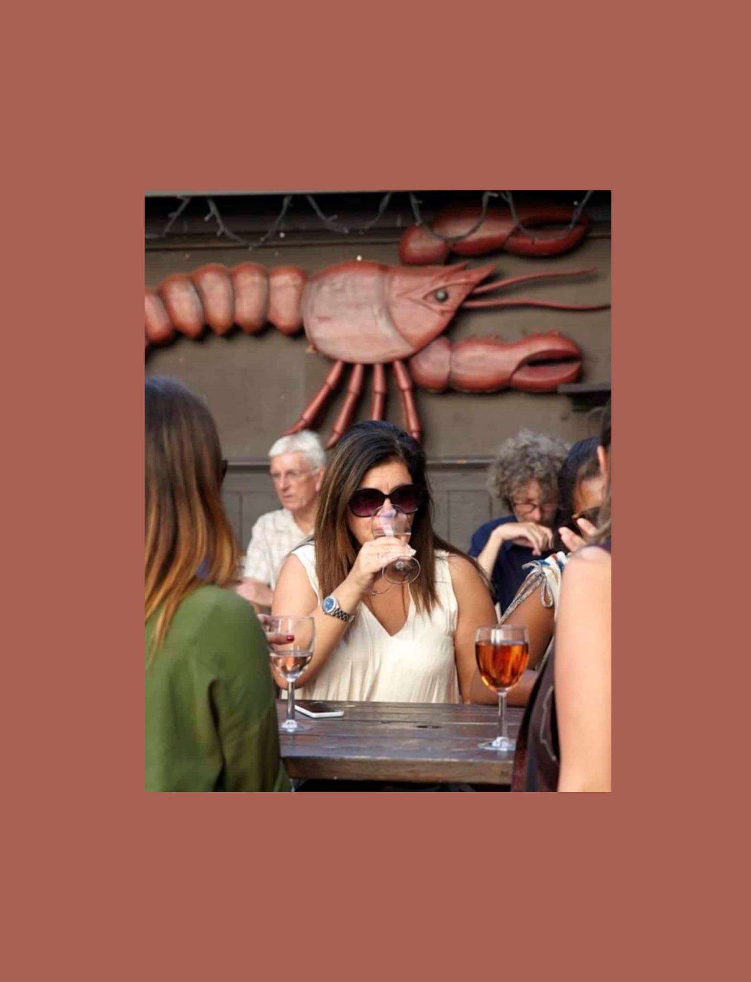 People drinking wine on a pub bench with a lobster on the wall in the background.