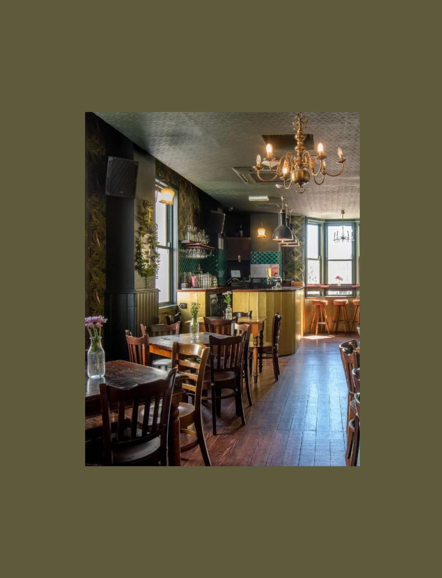 Inside of a bar with green patterned wallpaper, wooden tables and chairs.