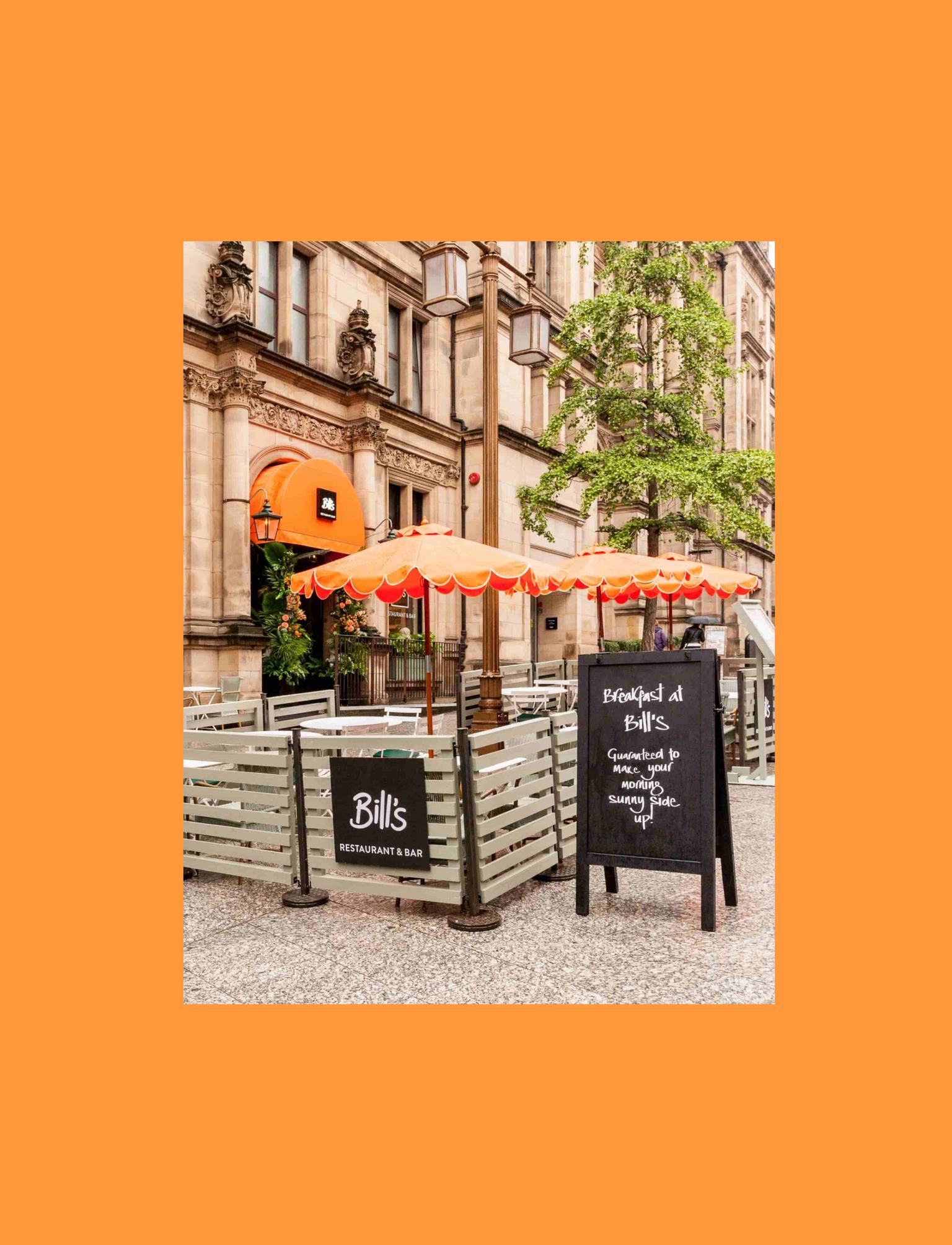 Street view of Bill's Restaurant &amp; Bar with outdoor seating and bright orange umbrellas.