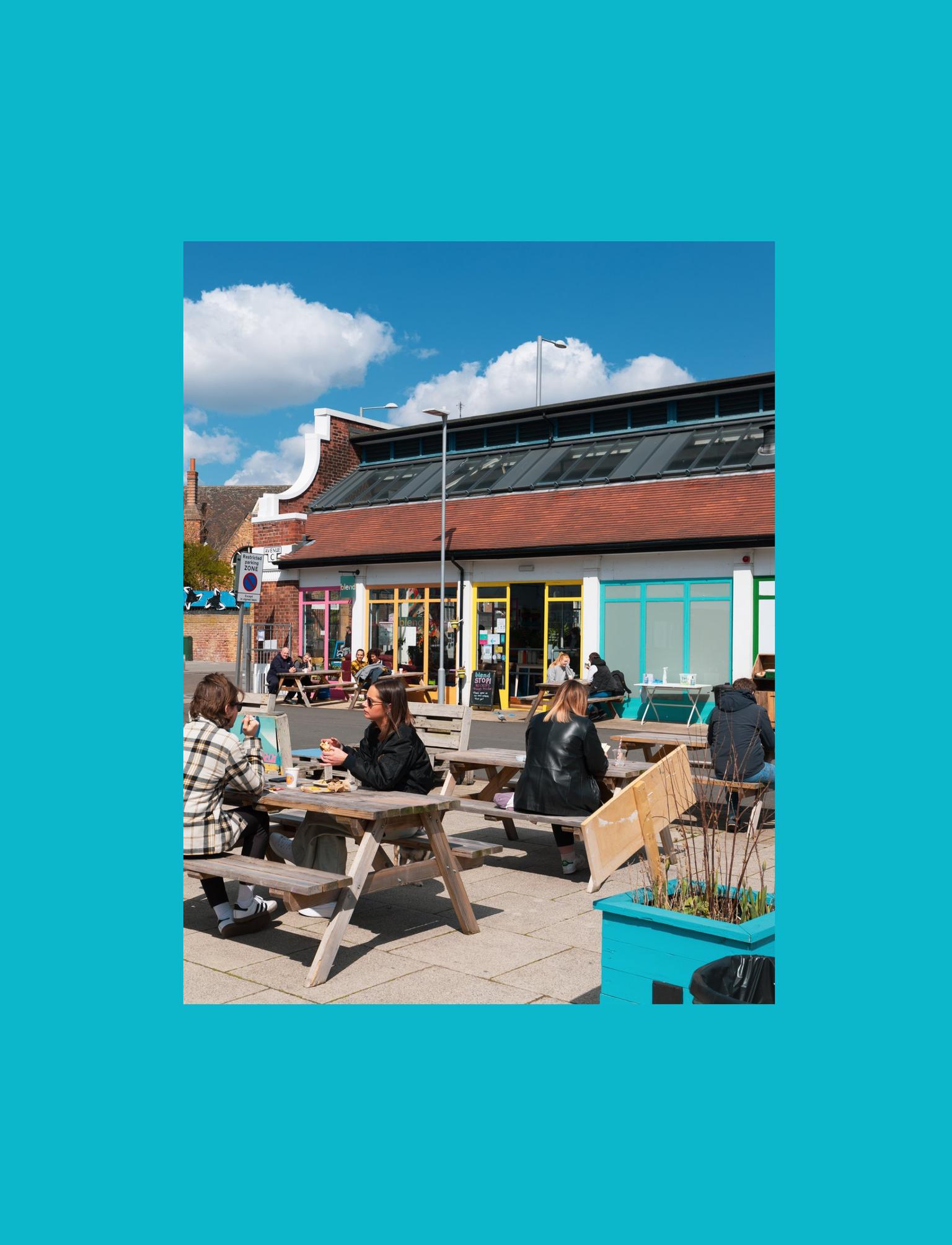 Outdoor café scene with people dining at picnic tables under a sunny sky.