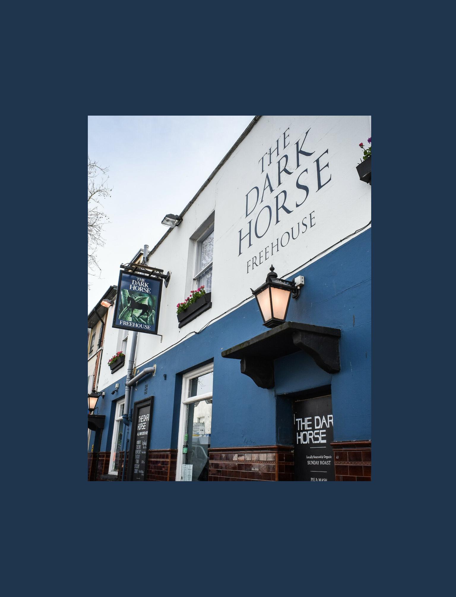 A blue and white painted front of a pub, with a black lantern hanging on the wall