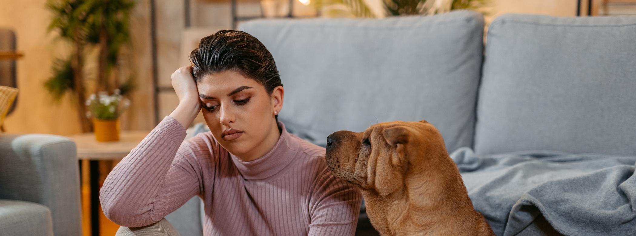 Person sitting on the floor with a stressed expression, next to a Shar Pei dog in a cozy living room.