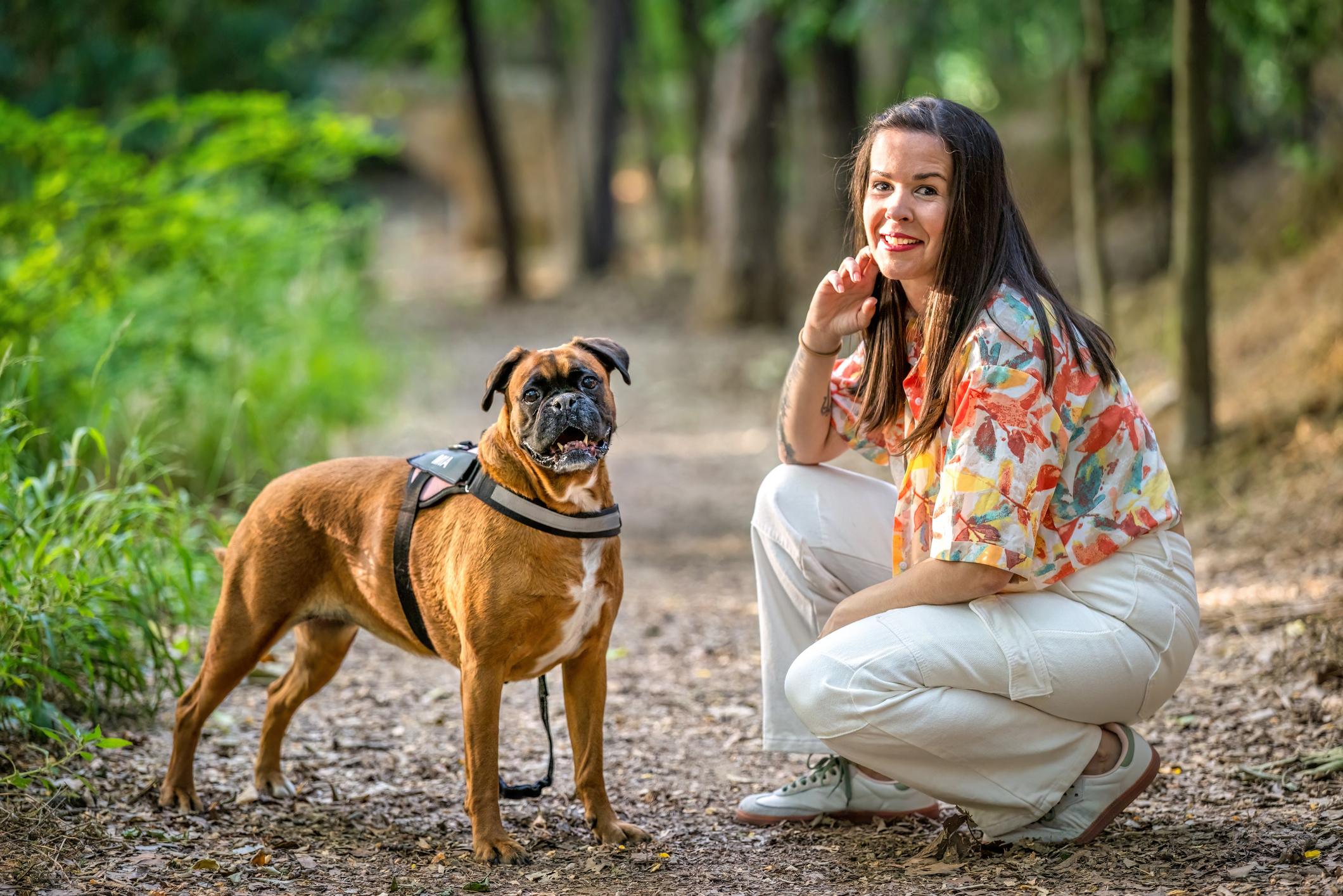 Image of a woman kneeling down next to a Boxer outside on a path in woodland