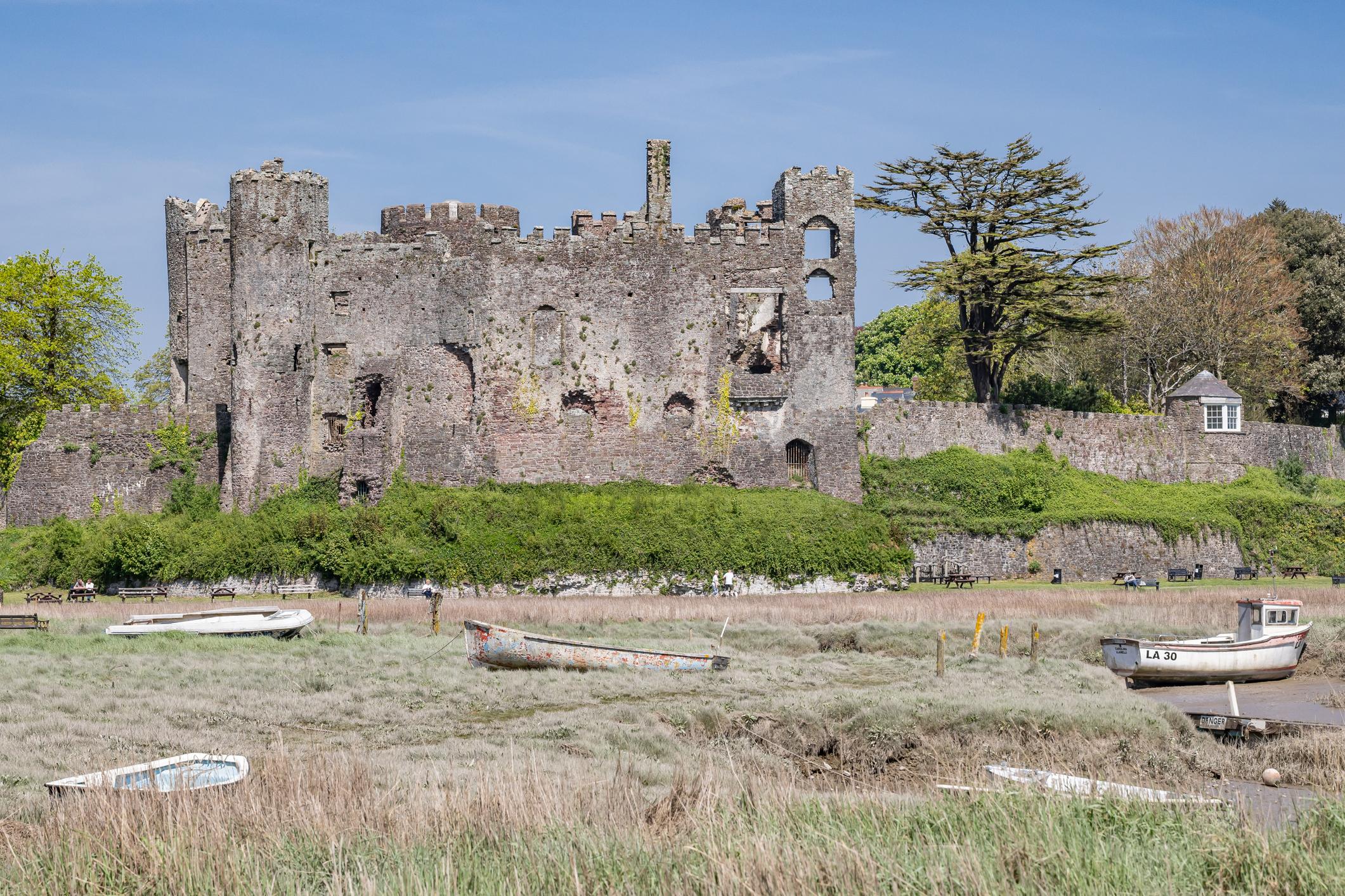 Image of Castle Laugharne on a bright day - there are old boats marooned in the estuary in front