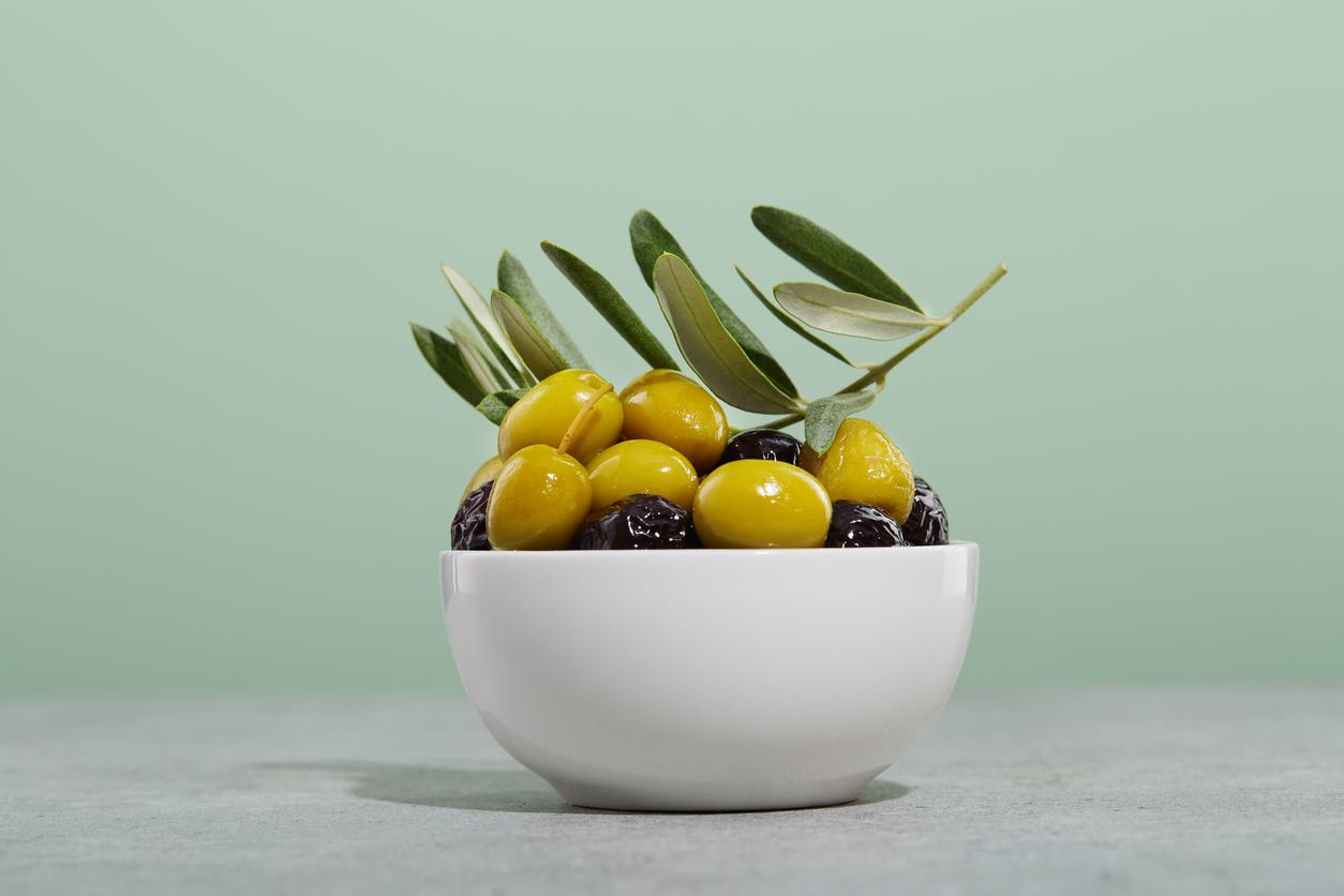 A white bowl filled with green and black olives and olive branches, set against a light green background.