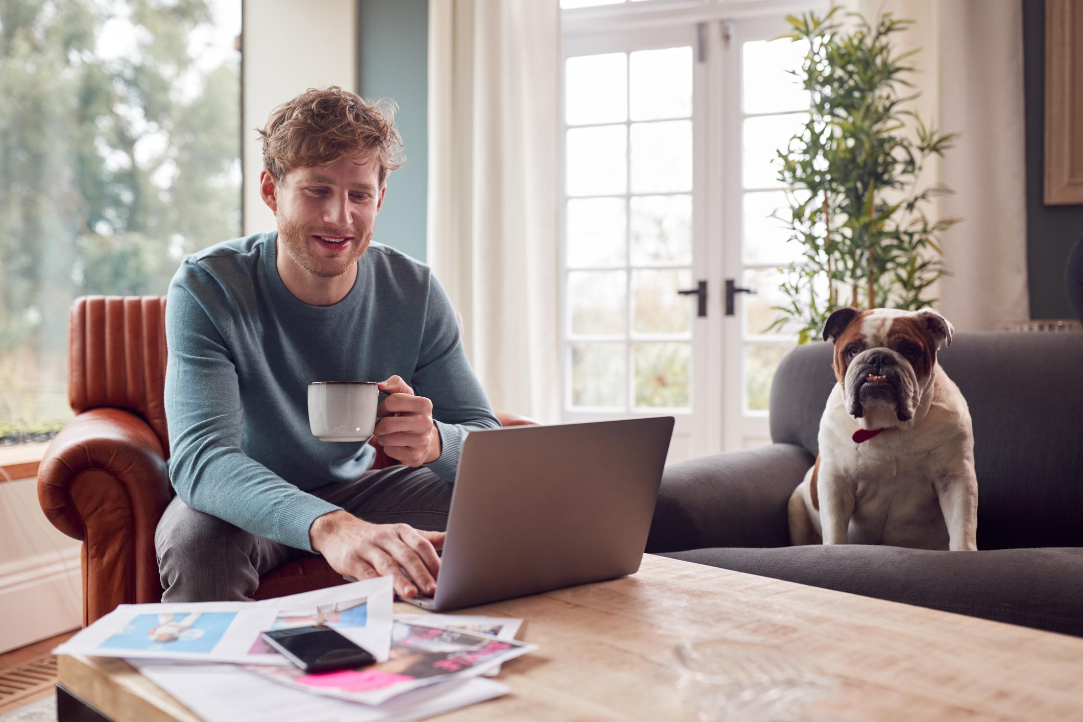A man sits with a cup of tea next to his Bulldog while working from home