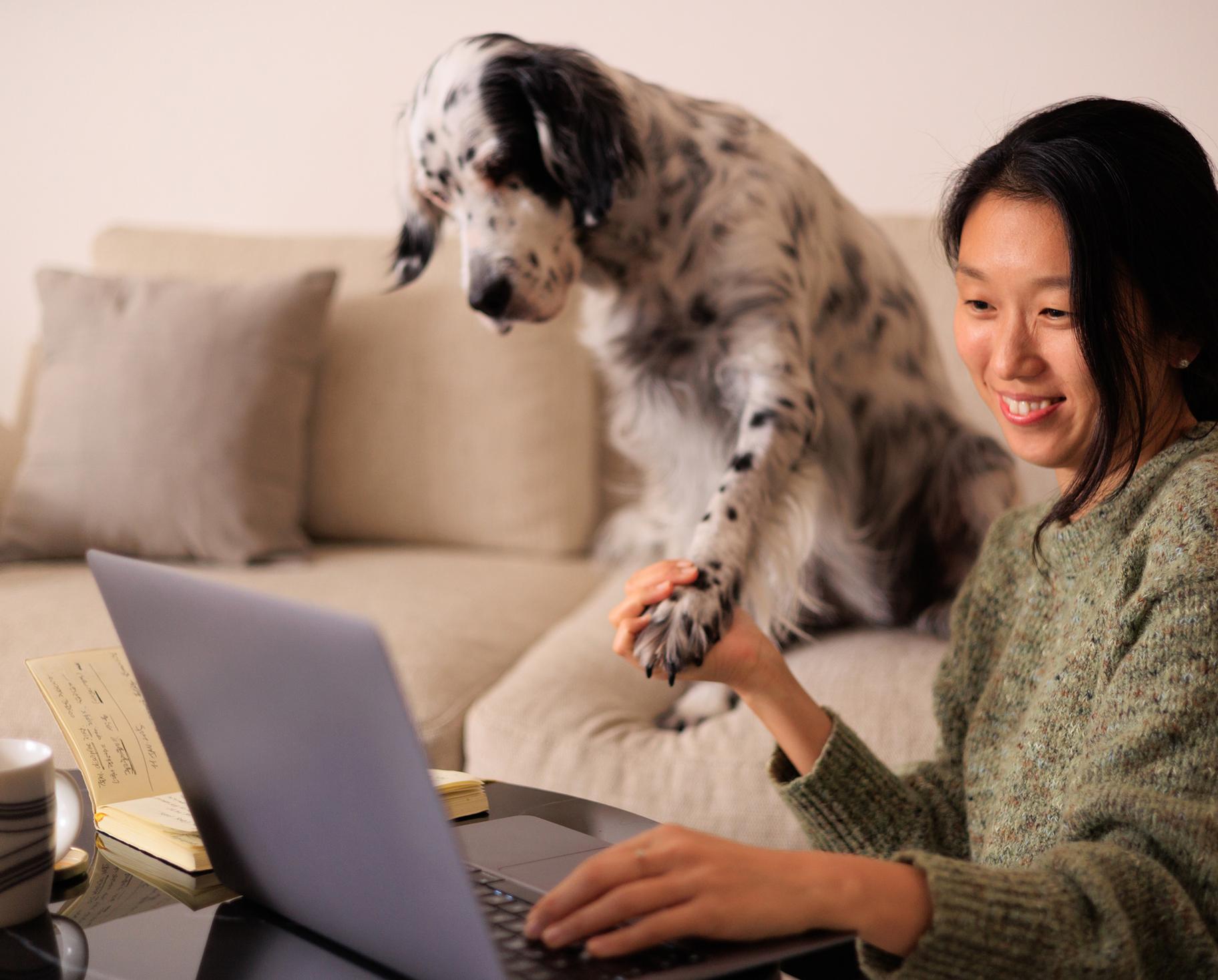 A woman shows off her black-and-white dog on her laptop camera, she is holding the dog's paw