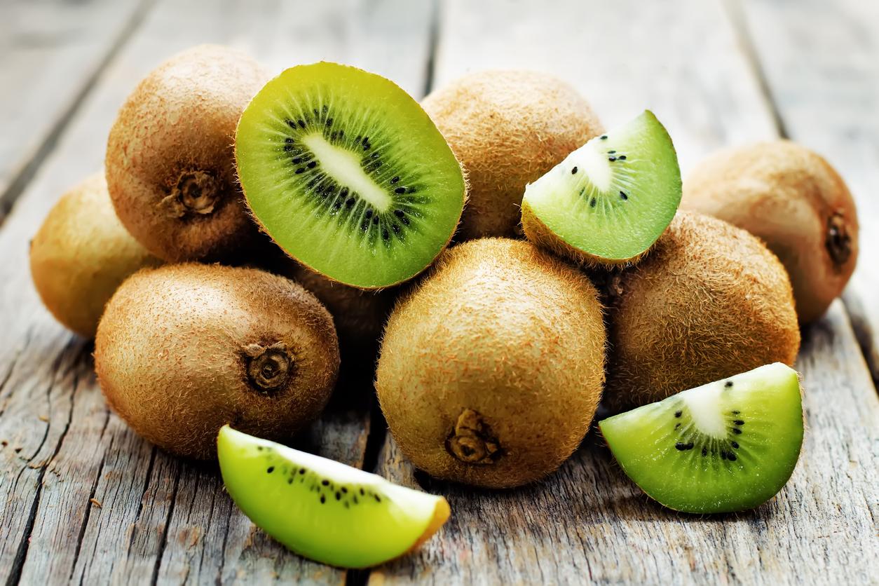 A pile of whole kiwis with a few slices showing vibrant green flesh and black seeds, set on a rustic wooden surface.