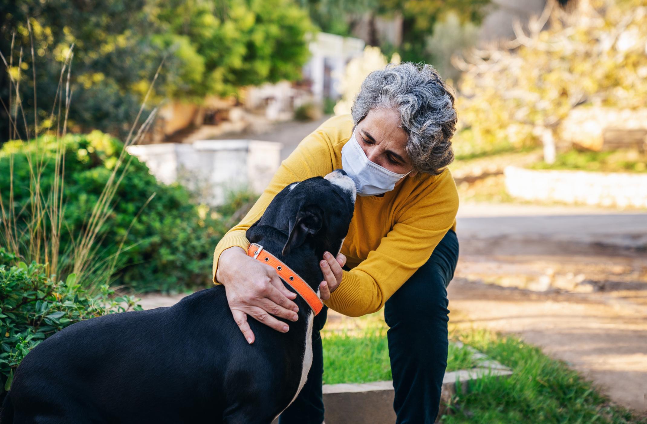 An older woman hugs her dog as she wears a face mask