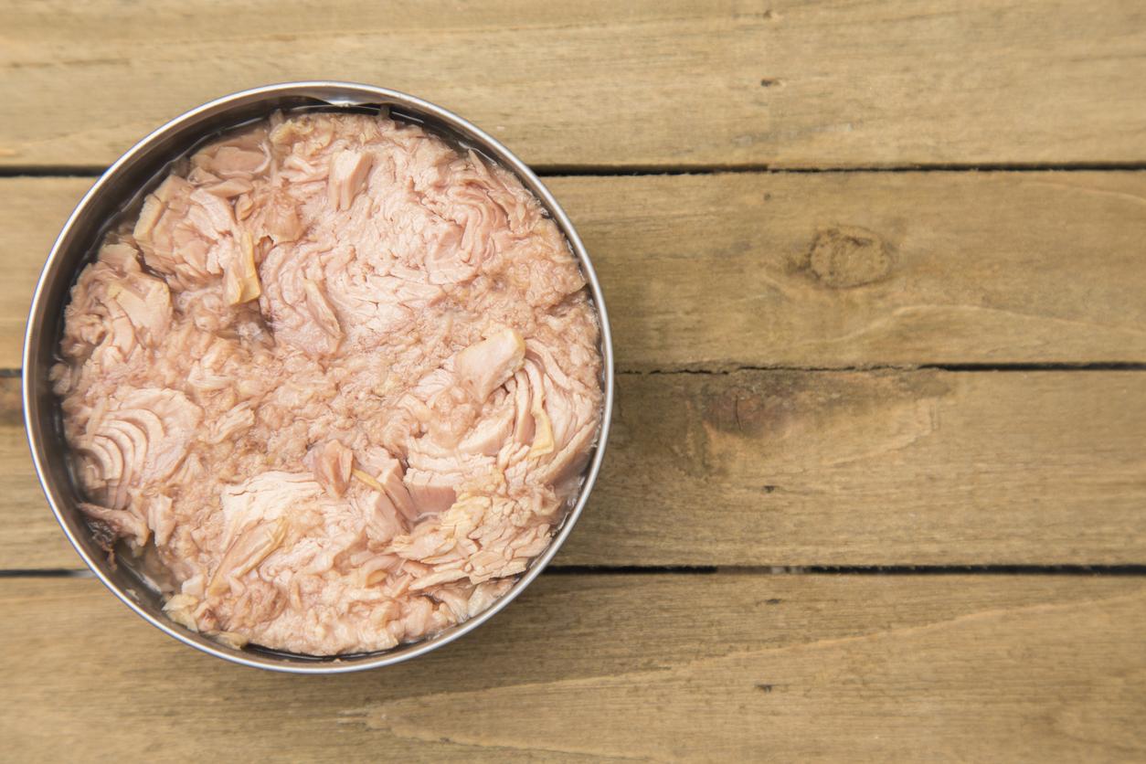 Open can of tuna on a wooden table, showing pink flaked fish inside.