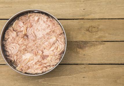 Open can of tuna on a wooden table, showing pink flaked fish inside.