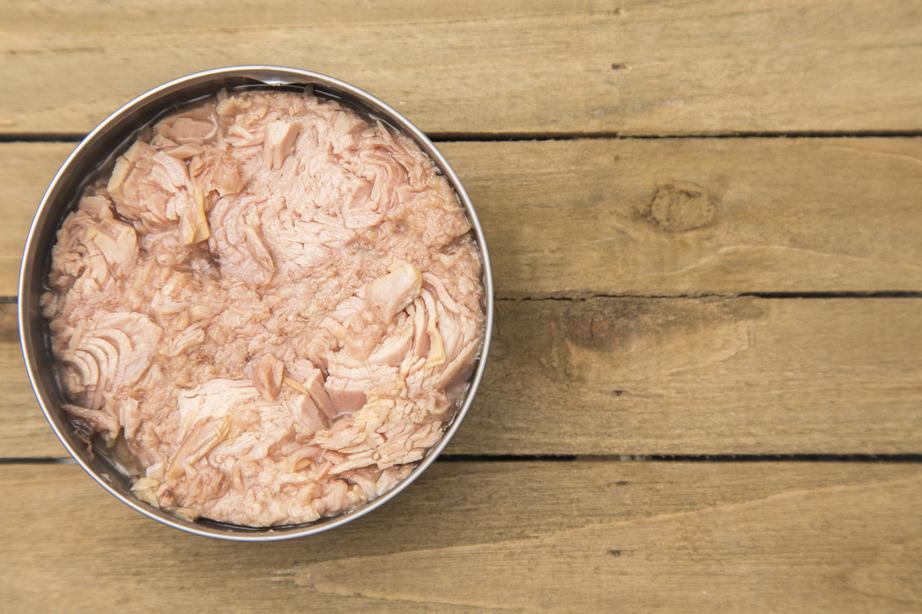 Open can of tuna on a wooden table, showing pink flaked fish inside.