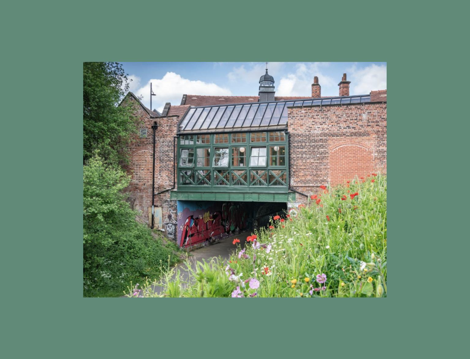 A quaint, green half-timbered building over an archway, surrounded by a vibrant wildflower foreground and lush greenery,