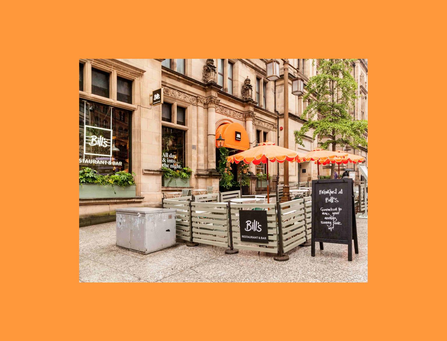 Street view of Bill's Restaurant &amp; Bar with outdoor seating and bright orange umbrellas.