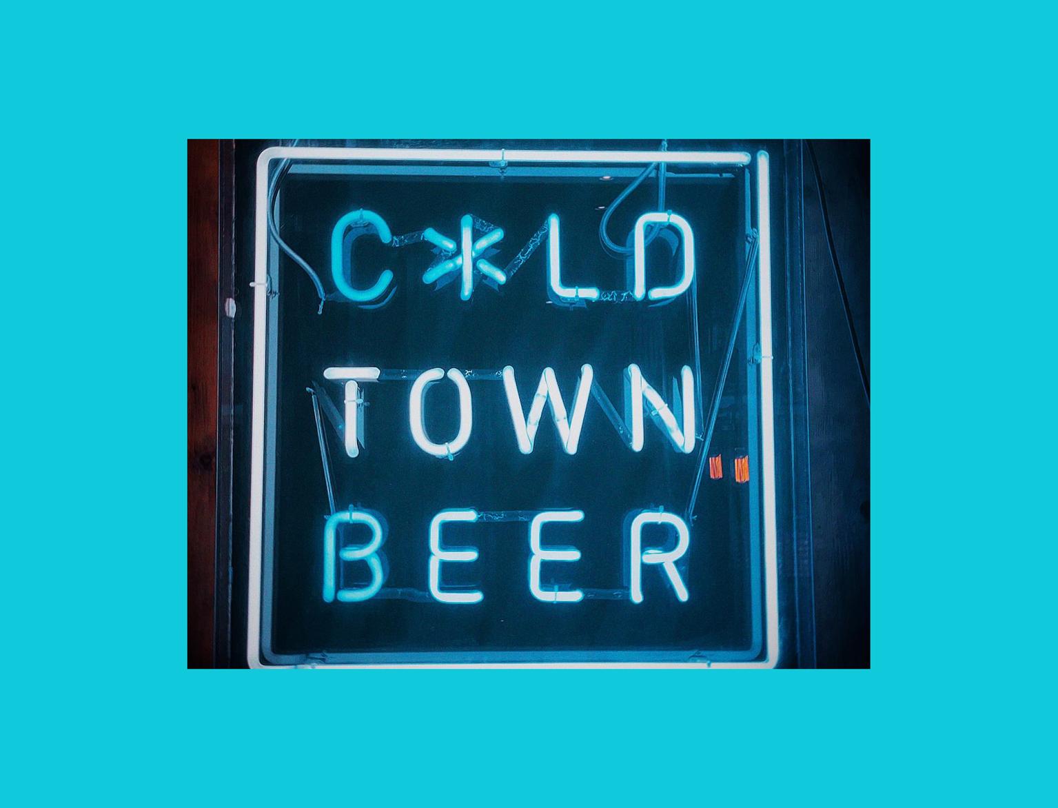 Neon sign reading "Cold Town Beer" mounted on a dark wooden wall, glowing in blue and white.