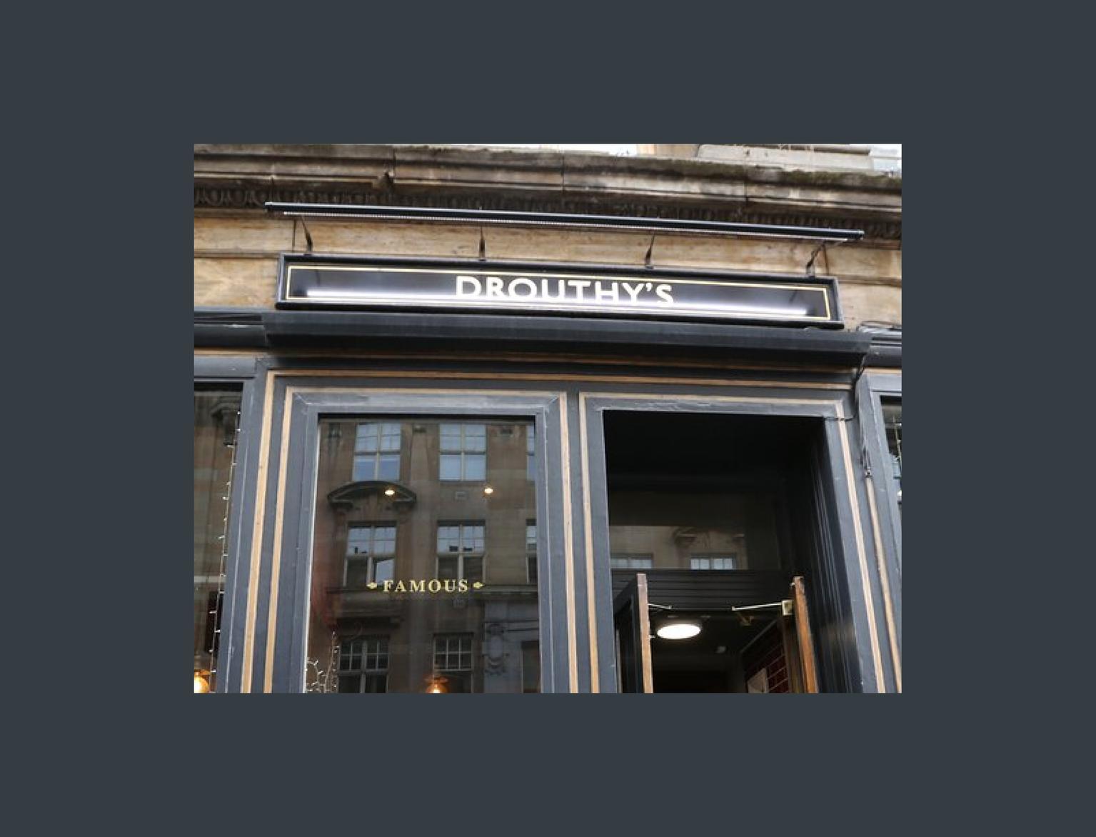 Facade of Drouthy's pub with gold signage, showcasing Scottish ales and spirits, in an elegant building.