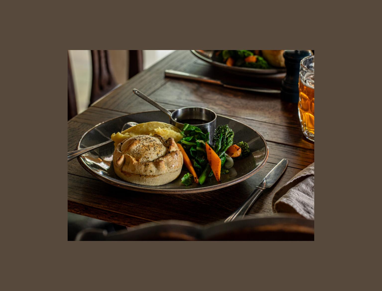 Pie, mash, vegetables and gravy on a plate, on a dark wood table.