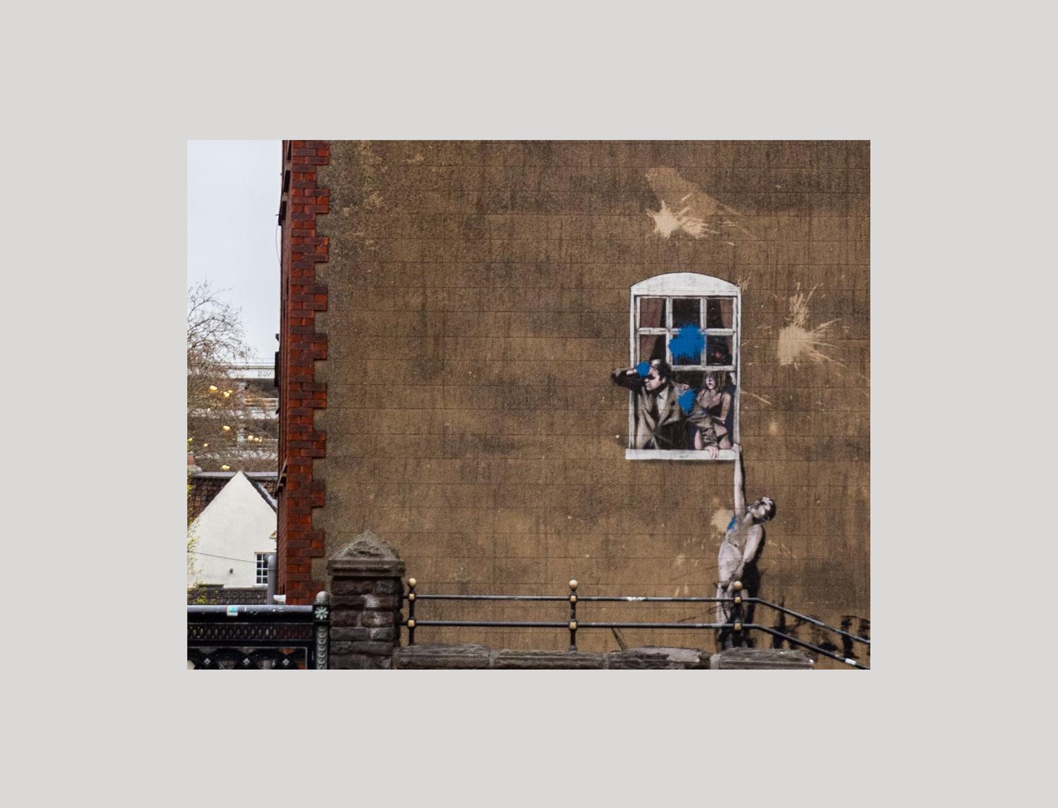 Bansky street art of man holding onto window ledge