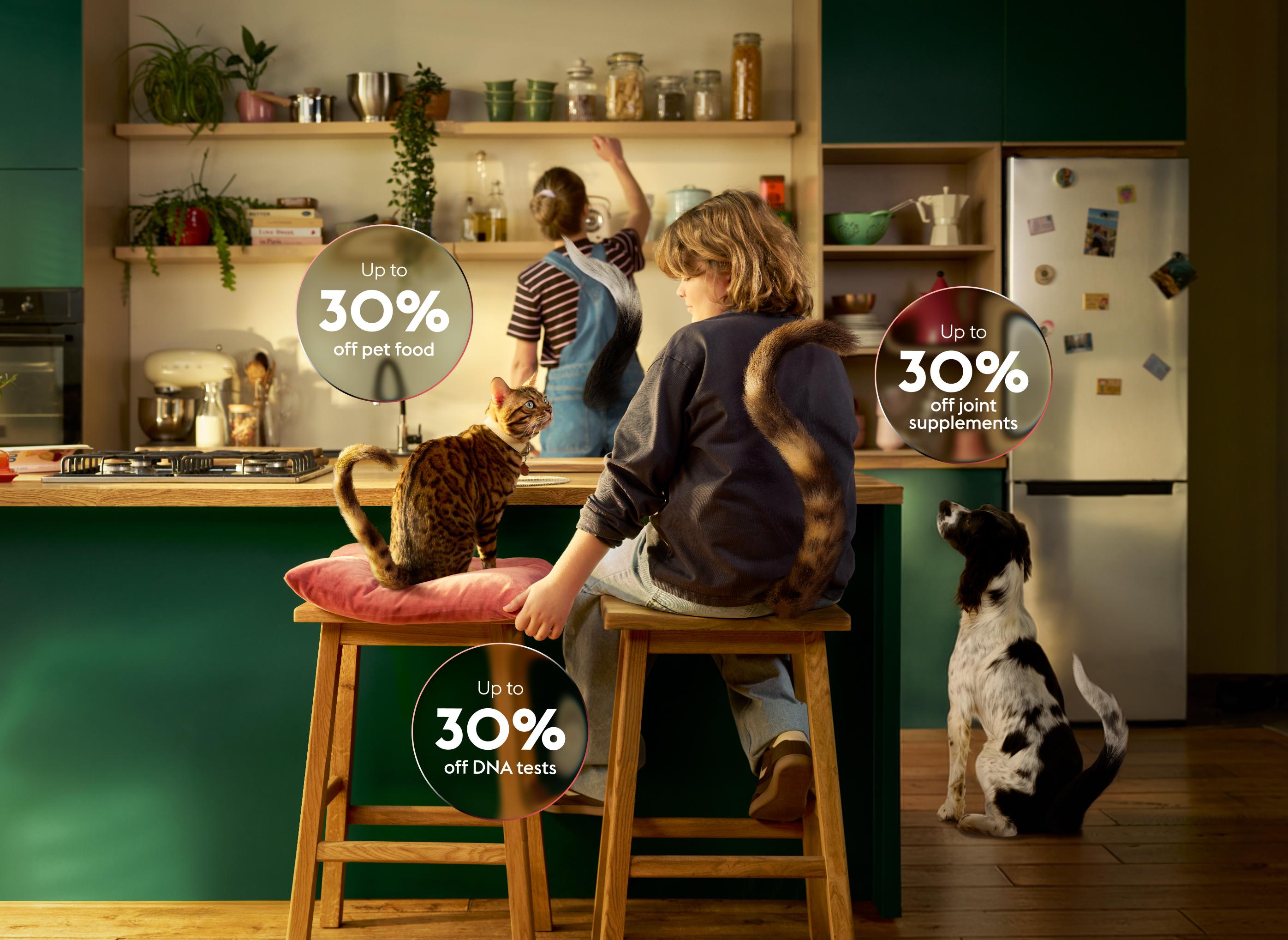 Boy and woman in kitchen with a cat and dog. Text bubbles highlight sales on pet food, DNA tests, and joint supplements.