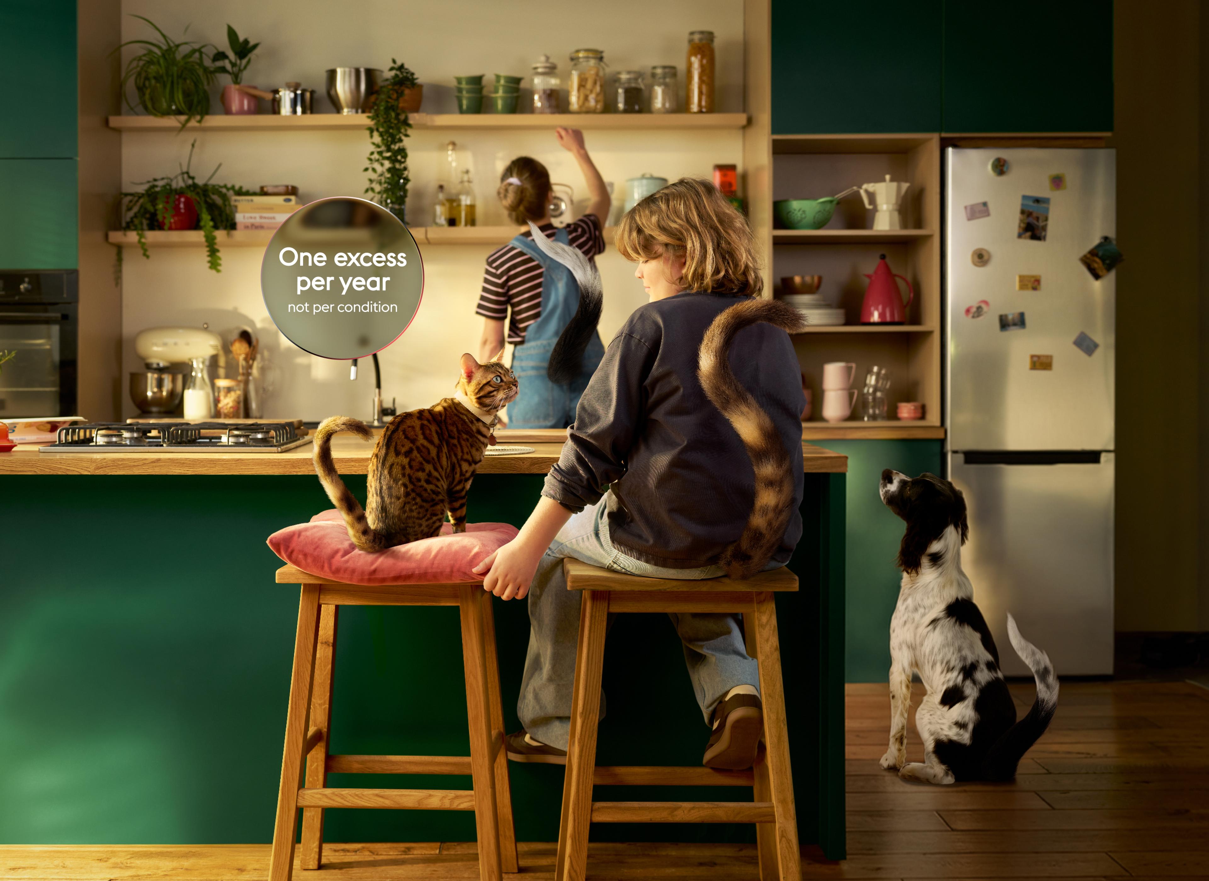 A woman and girl with tails sit in a kitchen; a dog sits nearby looking at the woman. Shelves and a fridge are in the background.