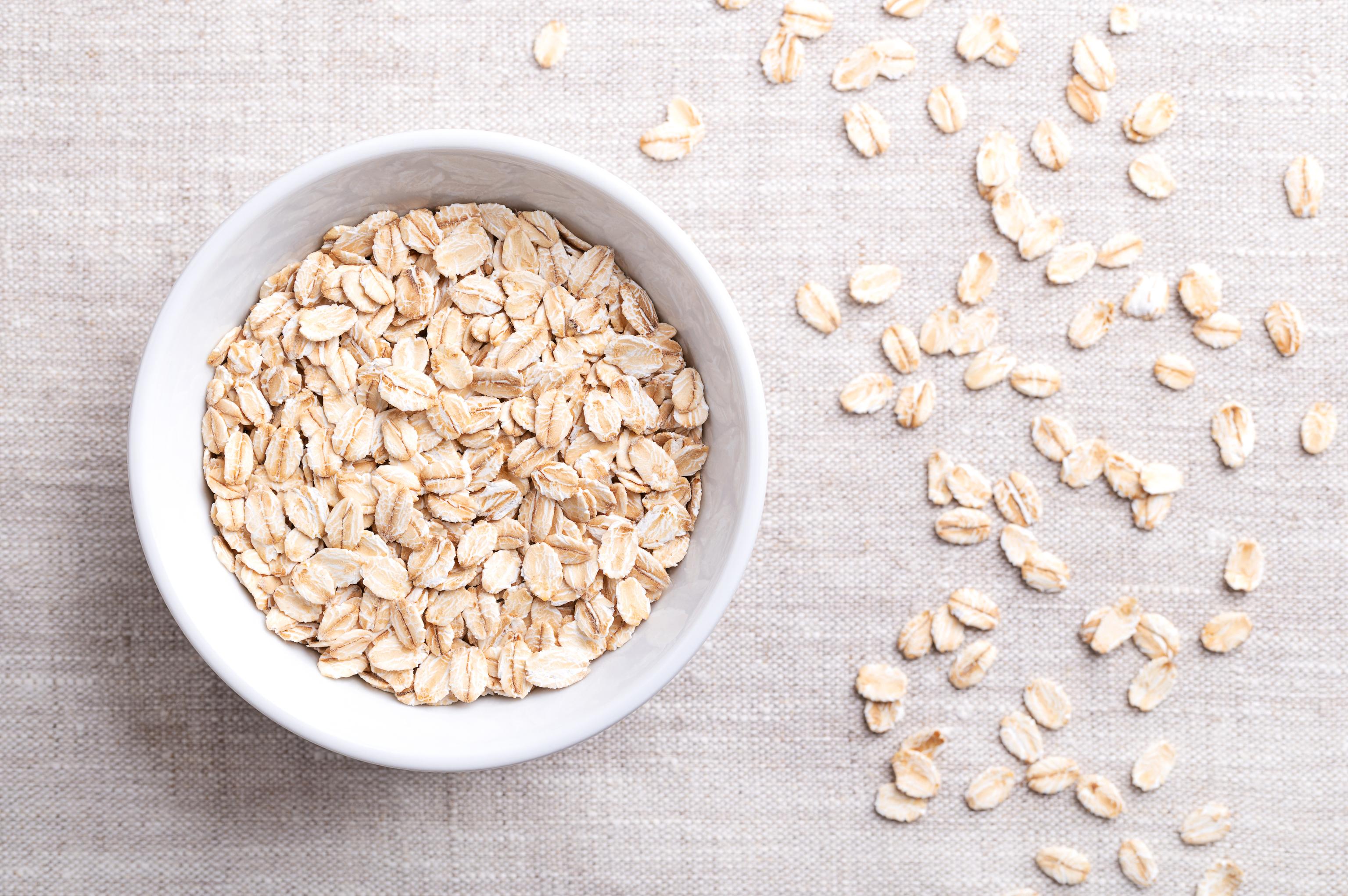 A bowl of raw oats with individual oats lined up next to it