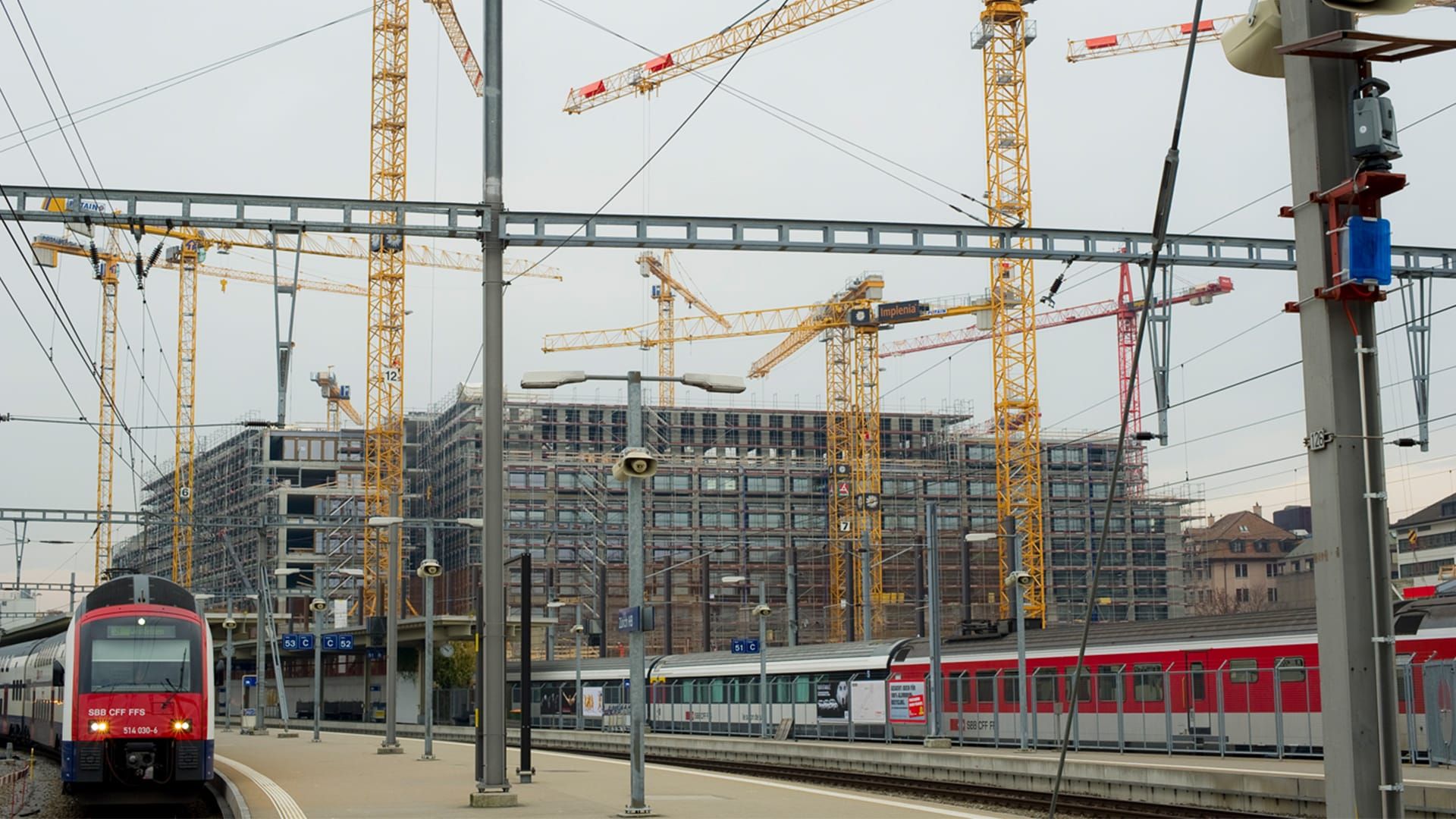 Mehrere gelbe Baukräne und Züge am Hauptbahnhof Zürich. Im Hintergrund entstehen die Gebäude der Europaallee. 