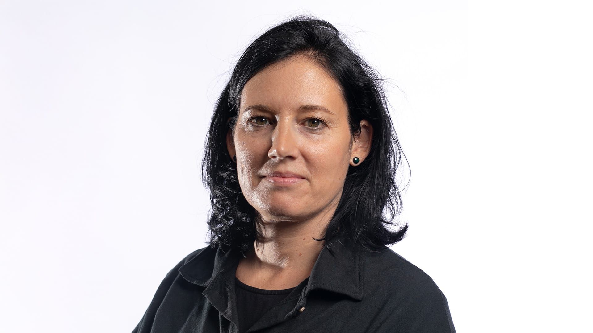 Auf dem Foto ist Nicole Hug porträtiert. Sie schaut in die Kamera. Ihre dunkelbraunen Haare sind leicht gewellt und reichen bis etwas über die Schultern. Sie trägt ein schwarzes Oberteil und darüber einen schwarzen Pullover.