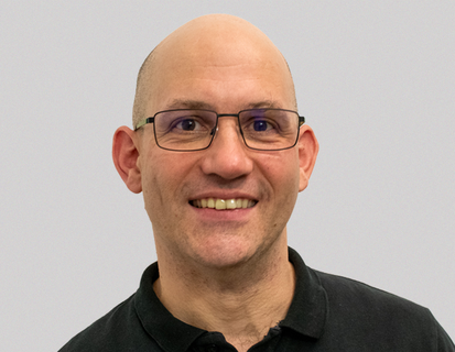 Porträt von Marc Taudien. Er trägt eine schwarze Brille und lächelt in die Kamera.