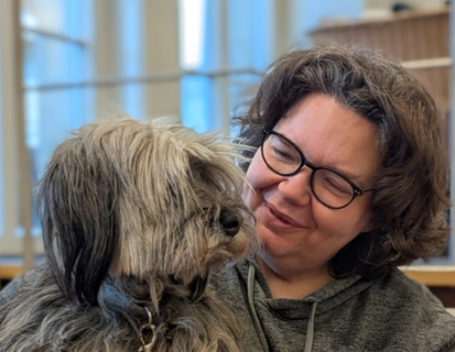 Porträt von Iris Andreska. Sie trägt eine schwarze Brille und schaut zu einem Hund, welchen sie im Arm hält.