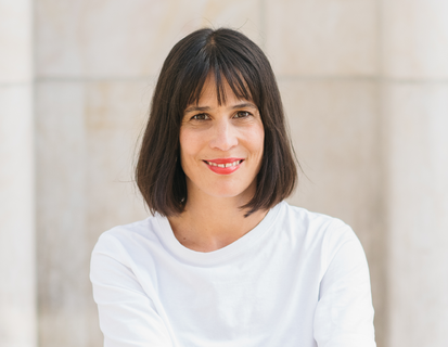 Porträt von Samantha Taylor. Sie hat braune Haare, die zu einem Bob geschnitten sind, trägt ein weisses T-Shirt und lächelt in die Kamera.