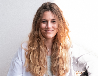 Porträt von Deborah Bischof. Sie hat lange, wellige blonde Haare und trägt ein helles Oberteil.