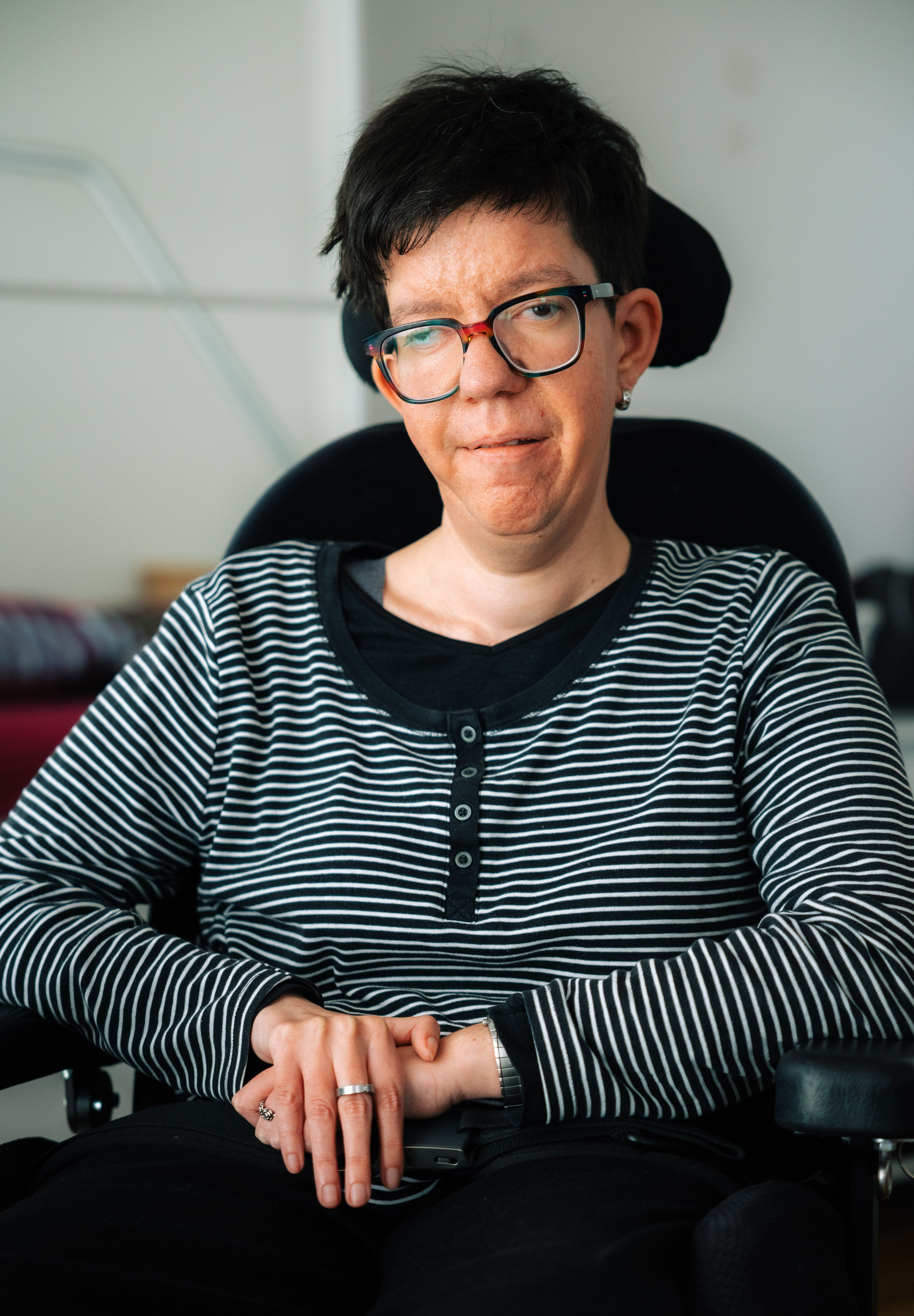 «Ich wusste gar nicht, wie das geht: jemanden anstellen», sagt Sandra Kropf. Ziemlich schnell musste sie das lernen. Bild: Surprise/David Fürst Sandra Kropf sitzt in einem Rollstuhl, trägt ein gestreiftes Hemd, hat die Hände gefaltet und blickt in die Kamera.