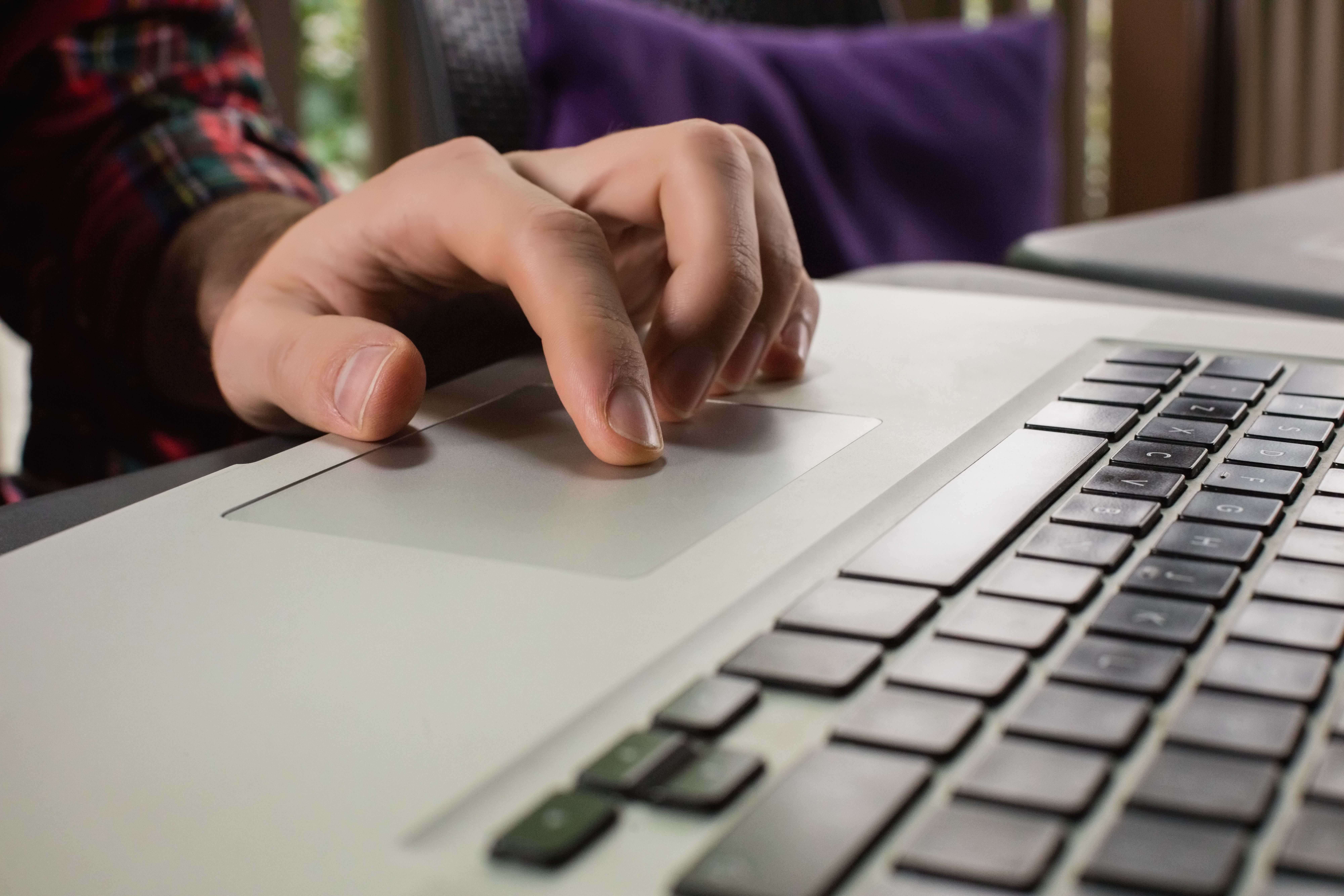 Viele Personen verzichten auf Sozialleistungen, da sie auf zahlreiche Barrieren stossen. Bild: Freepik Nahaufnahme der Hand einer Person, die das Trackpad auf der Tastatur eines silbernen Laptops bedient, mit unscharfem Hintergrund.