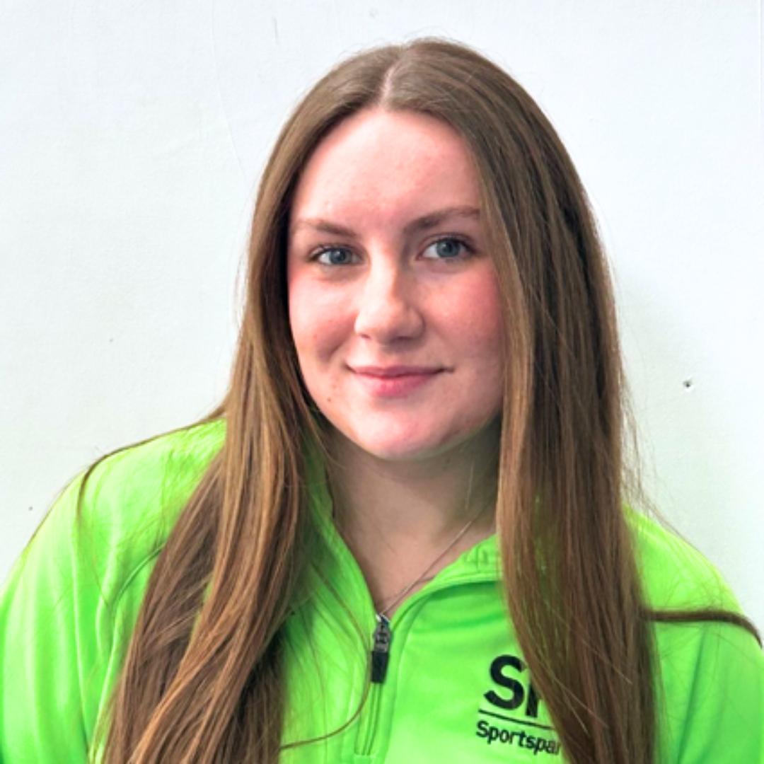 A young woman with long brown hair and blue eyes smiles while wearing a bright neon green quarter-zip jacket against a white background.