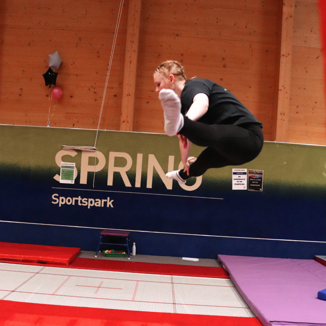 Girl jumping on an indoor trampoline doing a straddle jump.
