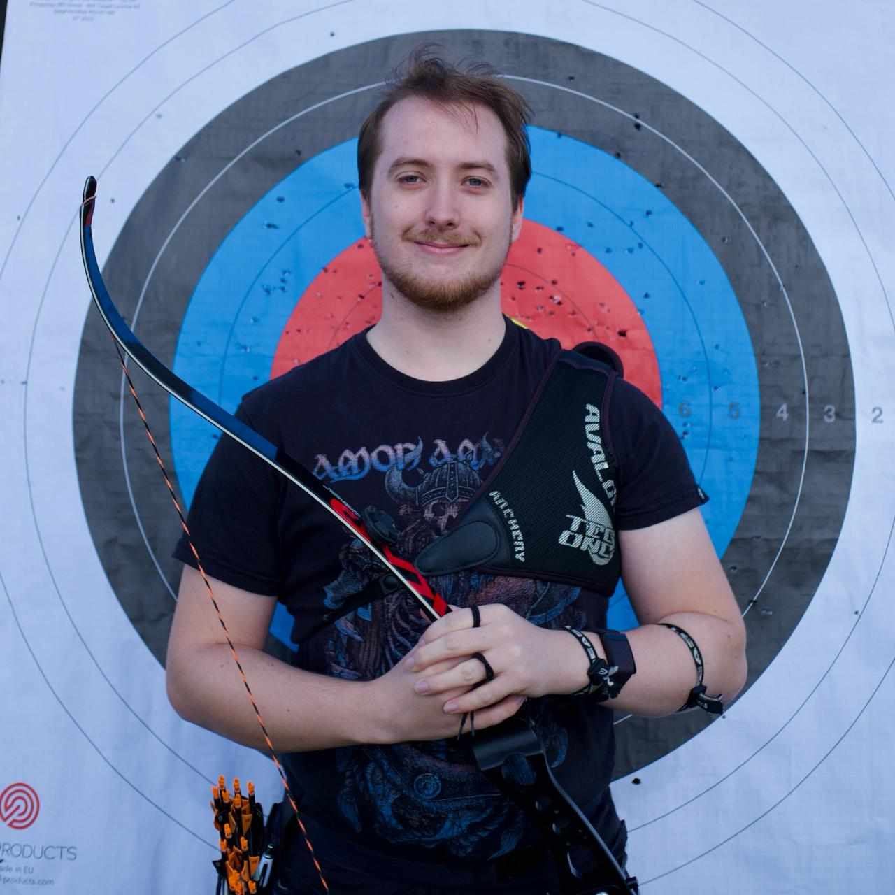 man with and and arrow in front of target smiling at the camera