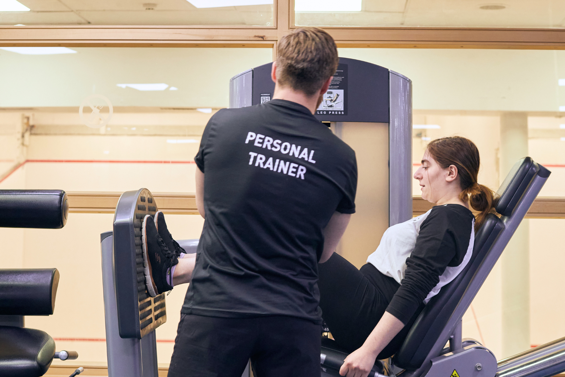 male personal trainer helping client on leg press machine in gym