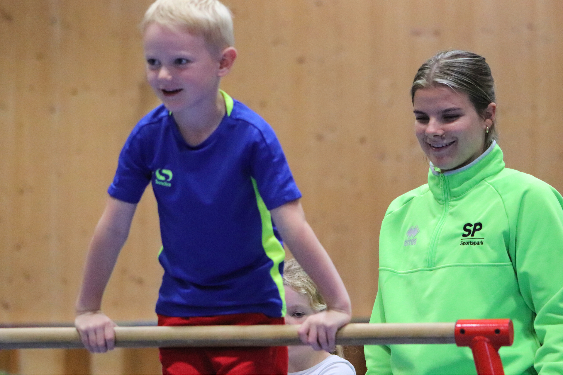 Young boy on gymnastics bars being watched by instructor.
