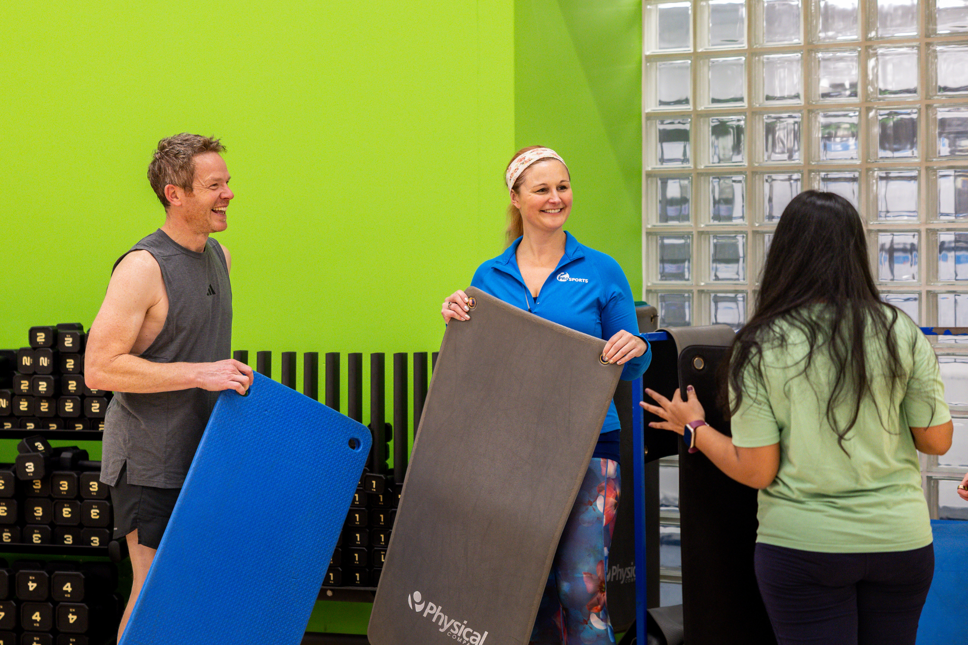 Two women and a man smiling and collecting yoga matt in dance studio.