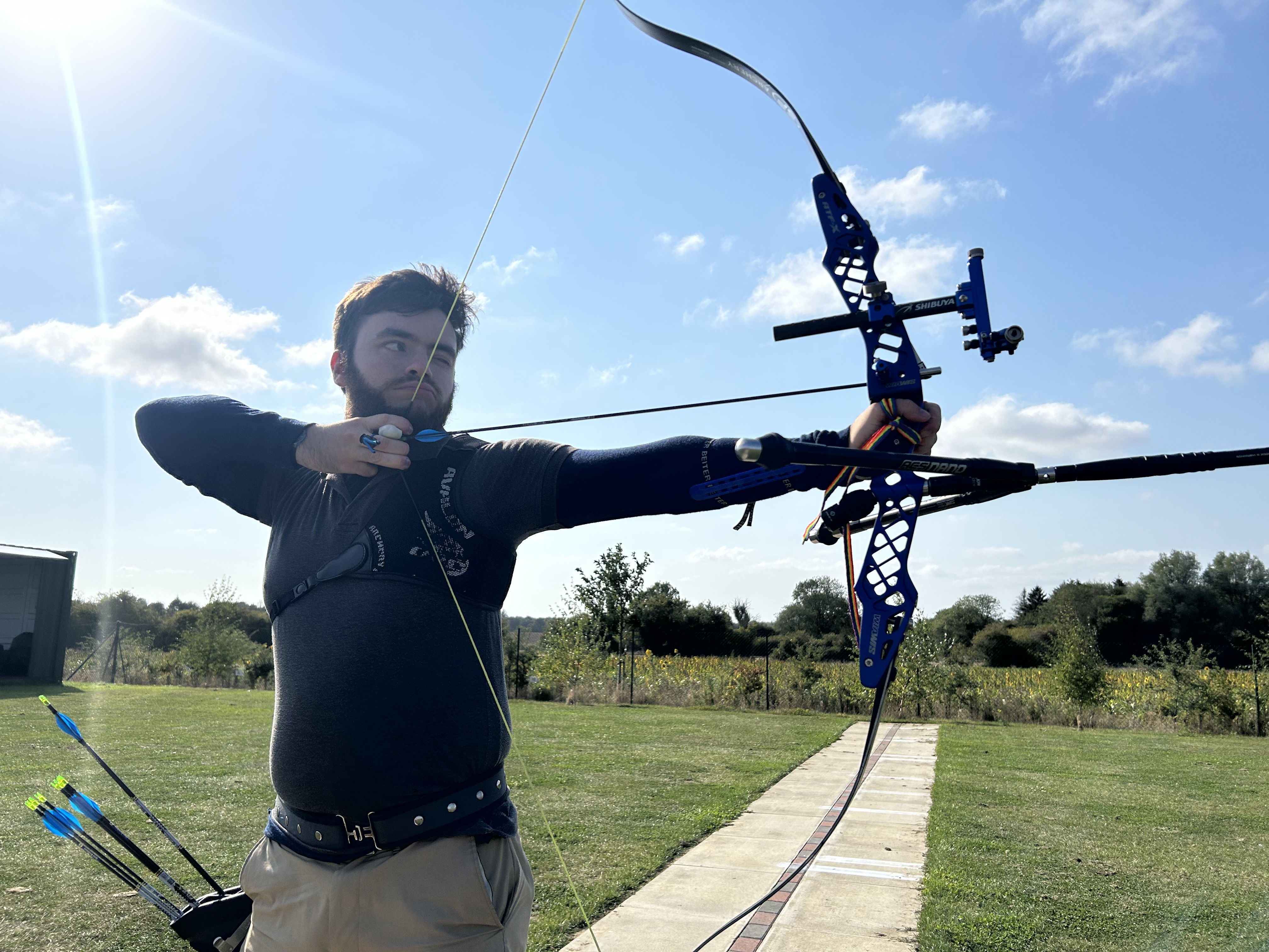 man drawing bowstring on bow and arrow outside on sunny day