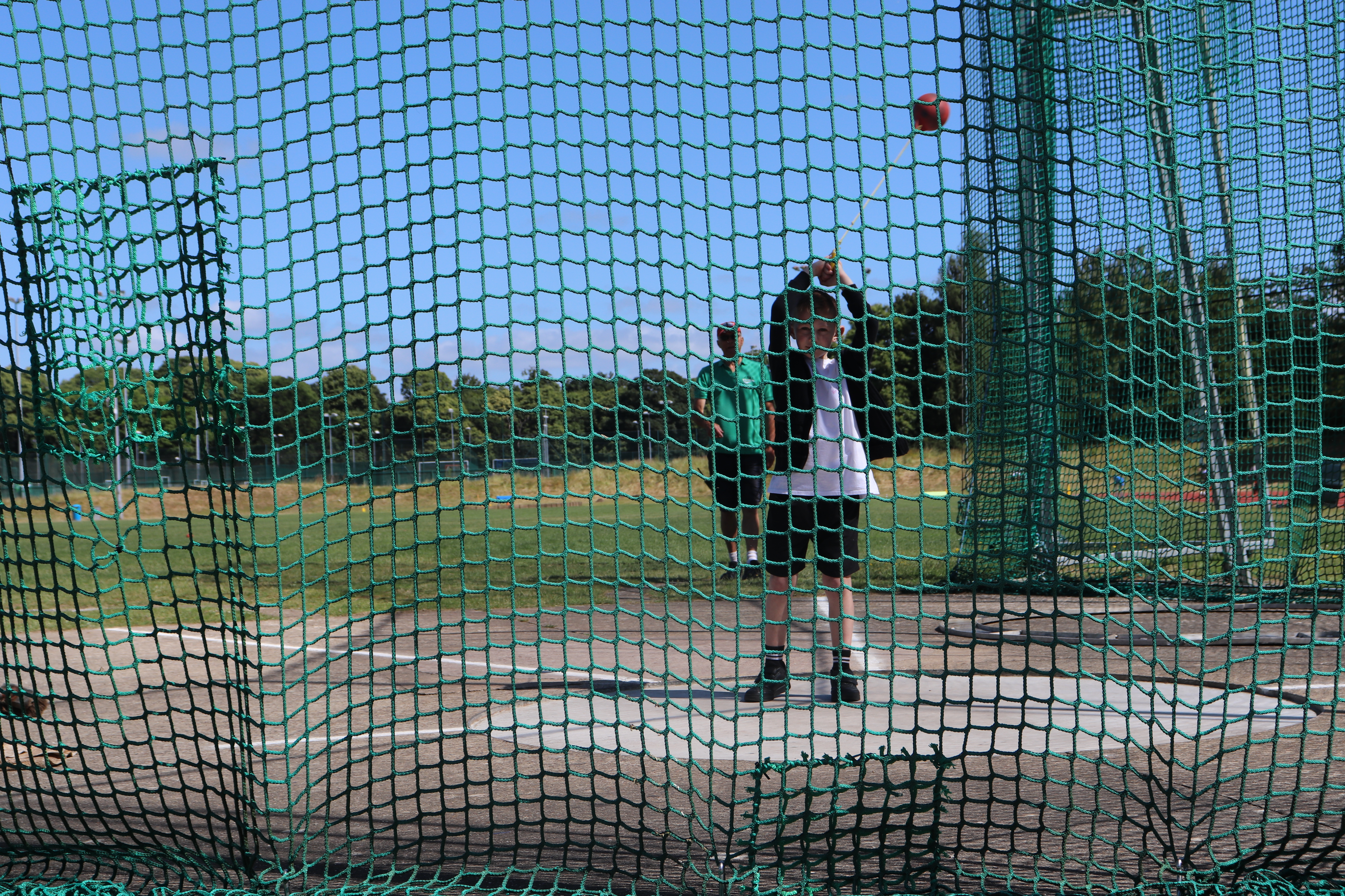 Small boy completes hammer throw inside hammer cage.