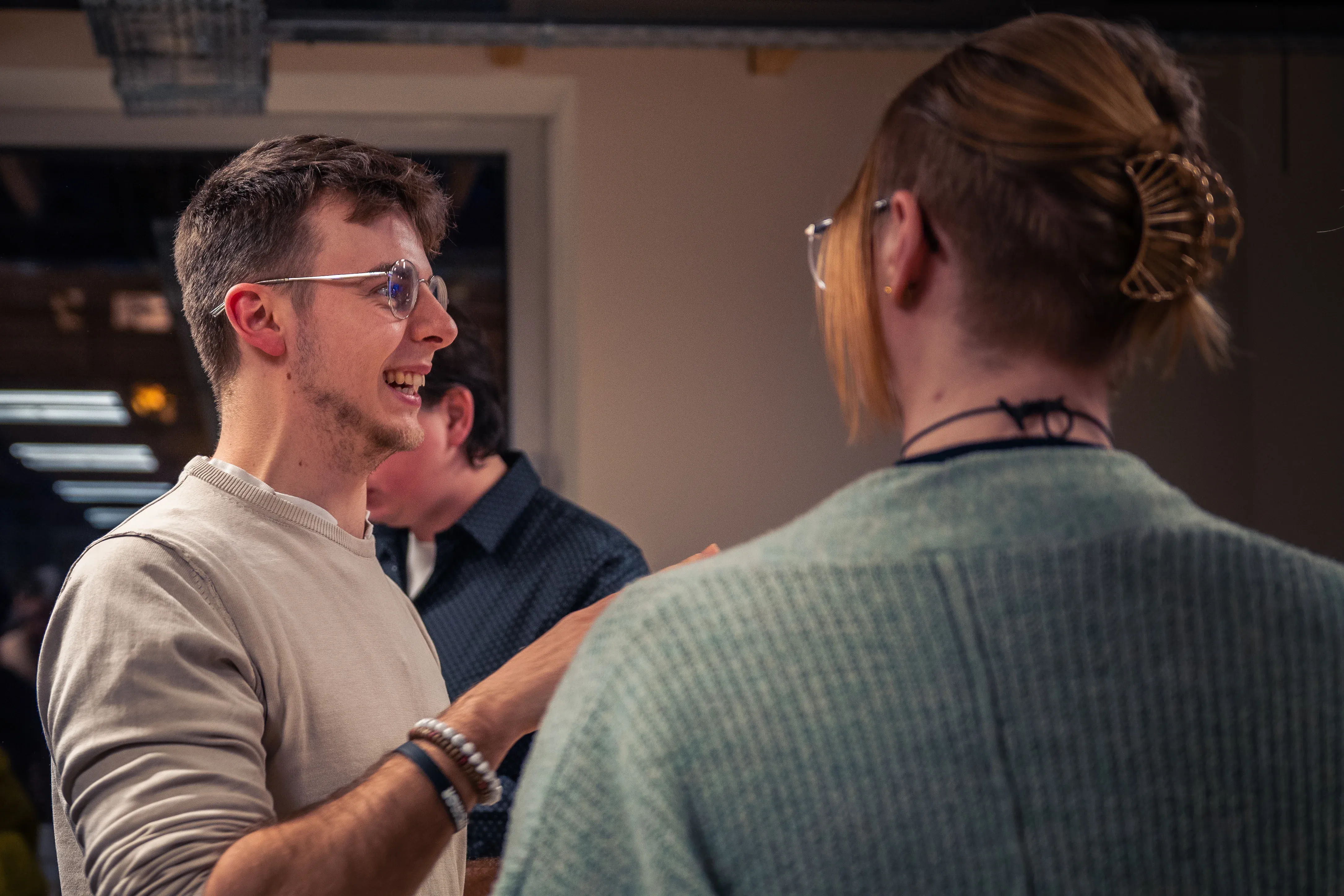 Two people engaged in a lively conversation indoors. One is facing the camera, gesturing with enthusiasm, while the other listens attentively.