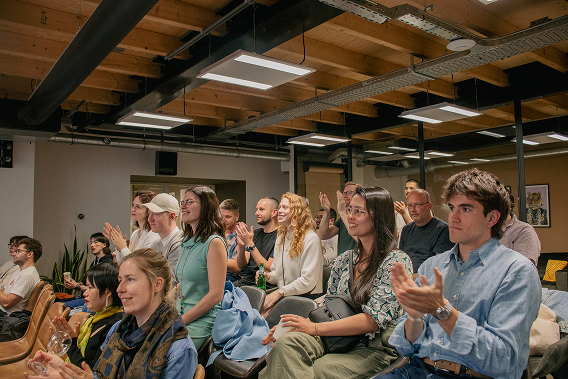 A diverse group of people at the design meetup, attentively watching and applauding something off-camera.