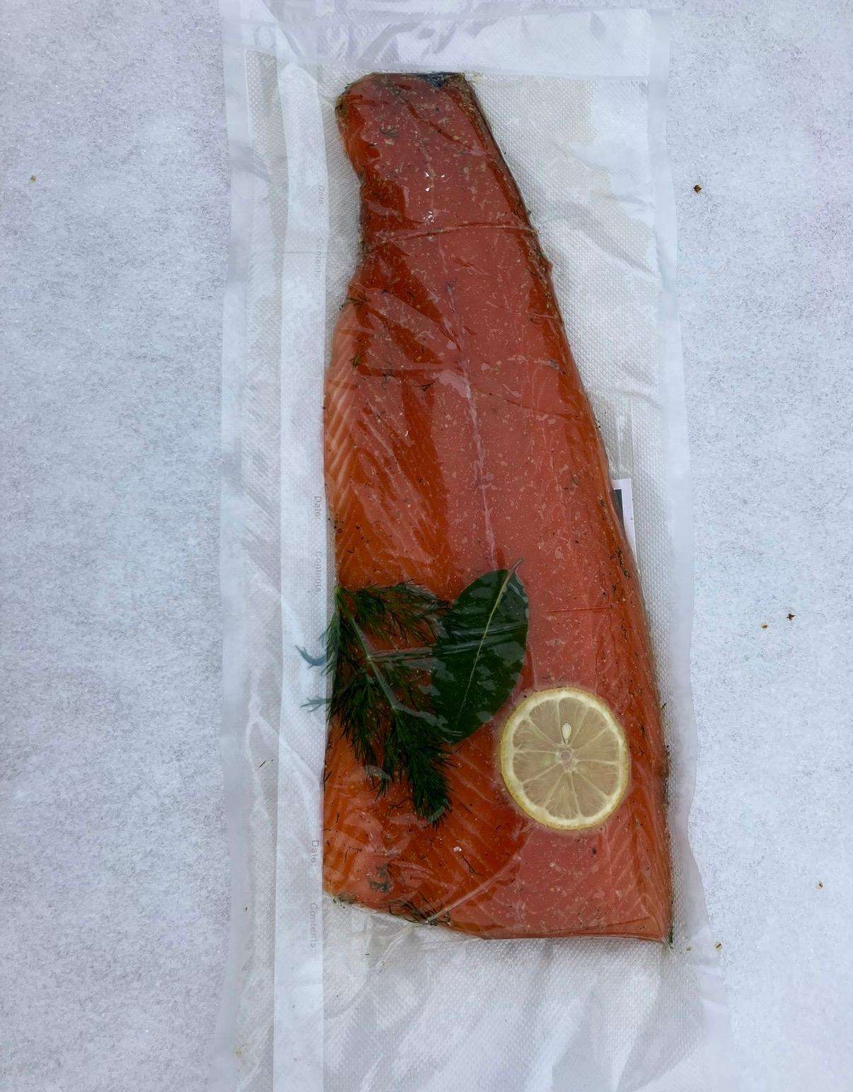 Vakuumverpacktes Stück Lachs mit Dill und Zitronenscheibe auf eisigem Untergrund.