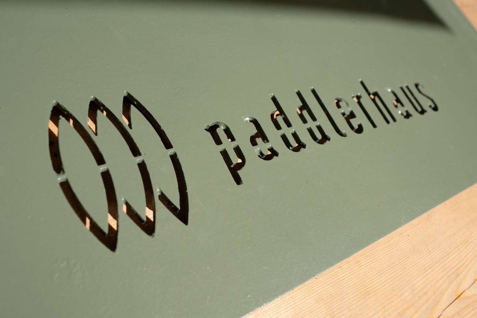 Paddlerhaus-Logo mit drei Paddelblättern, ausgelasert in einem grünen Schirmständer