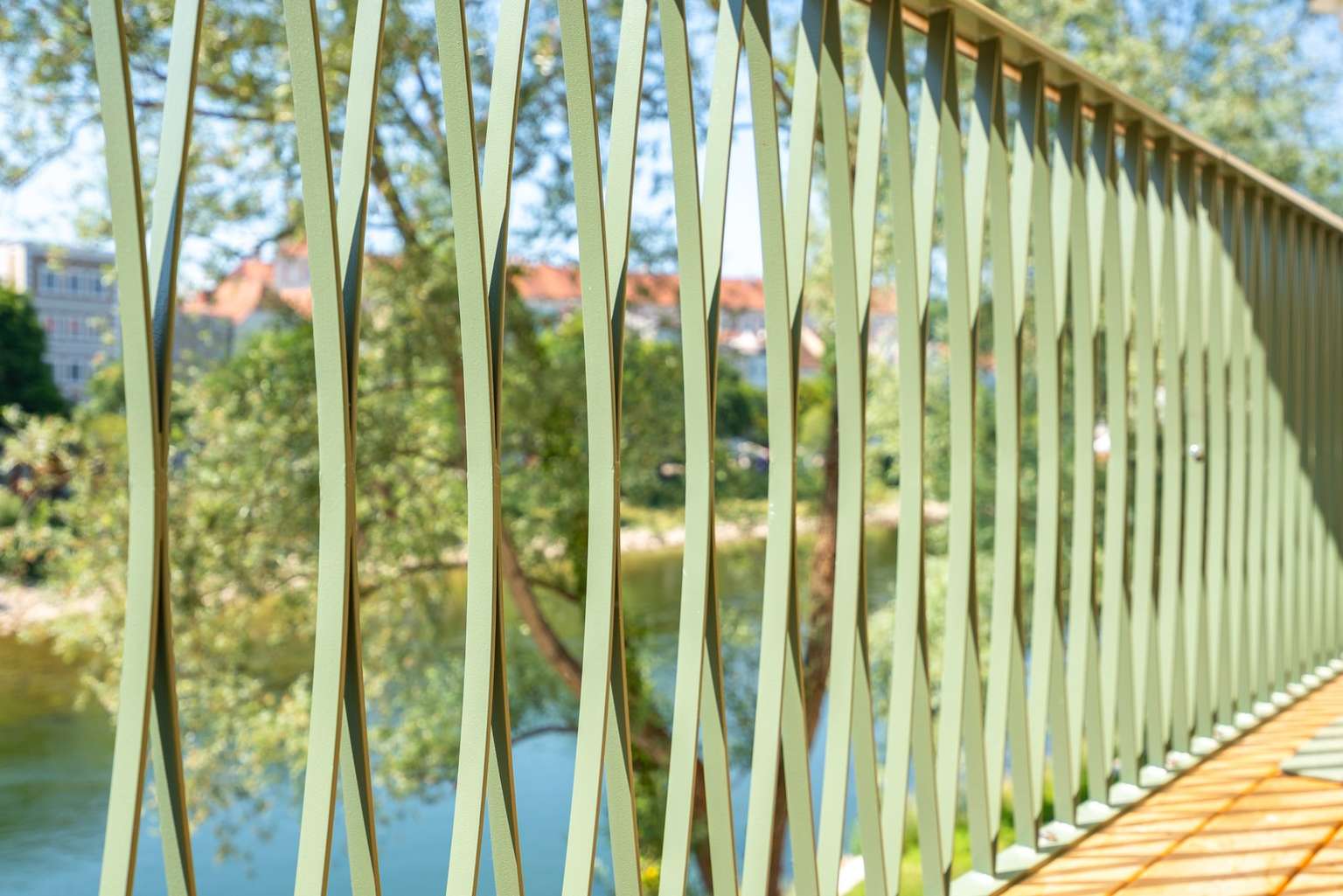 Grünes Geländer mit geschwungenen Paddelformen an der Terrasse des Paddlerhaus, im Hintergrund die Enns