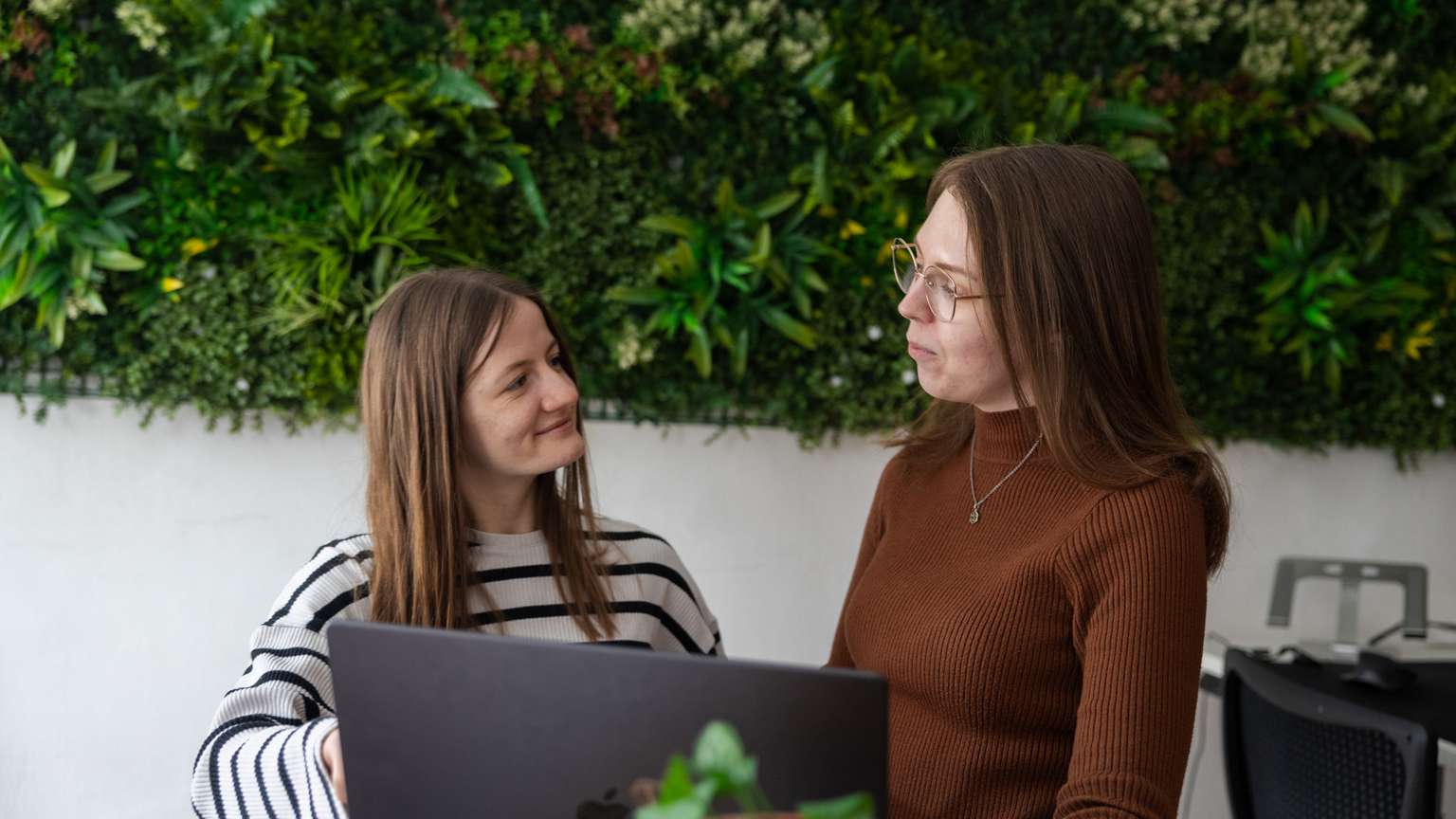Zwei junge Frauen reden vor einer begrünten Wand.