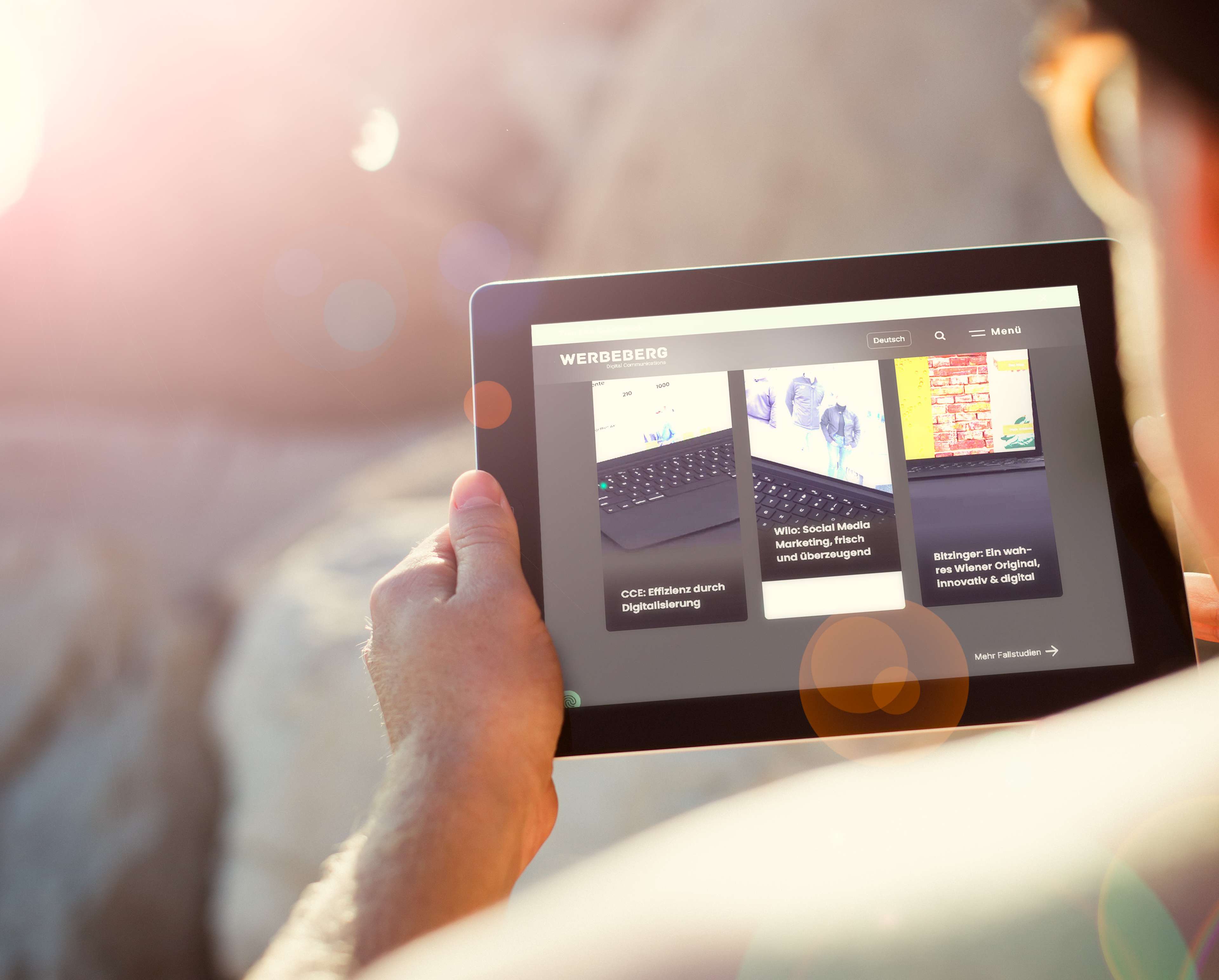 Eine Person hält ein Tablet in der Hand, dass die Werbeberg Webseite bei hellen Lichtverhältnissen zeigt