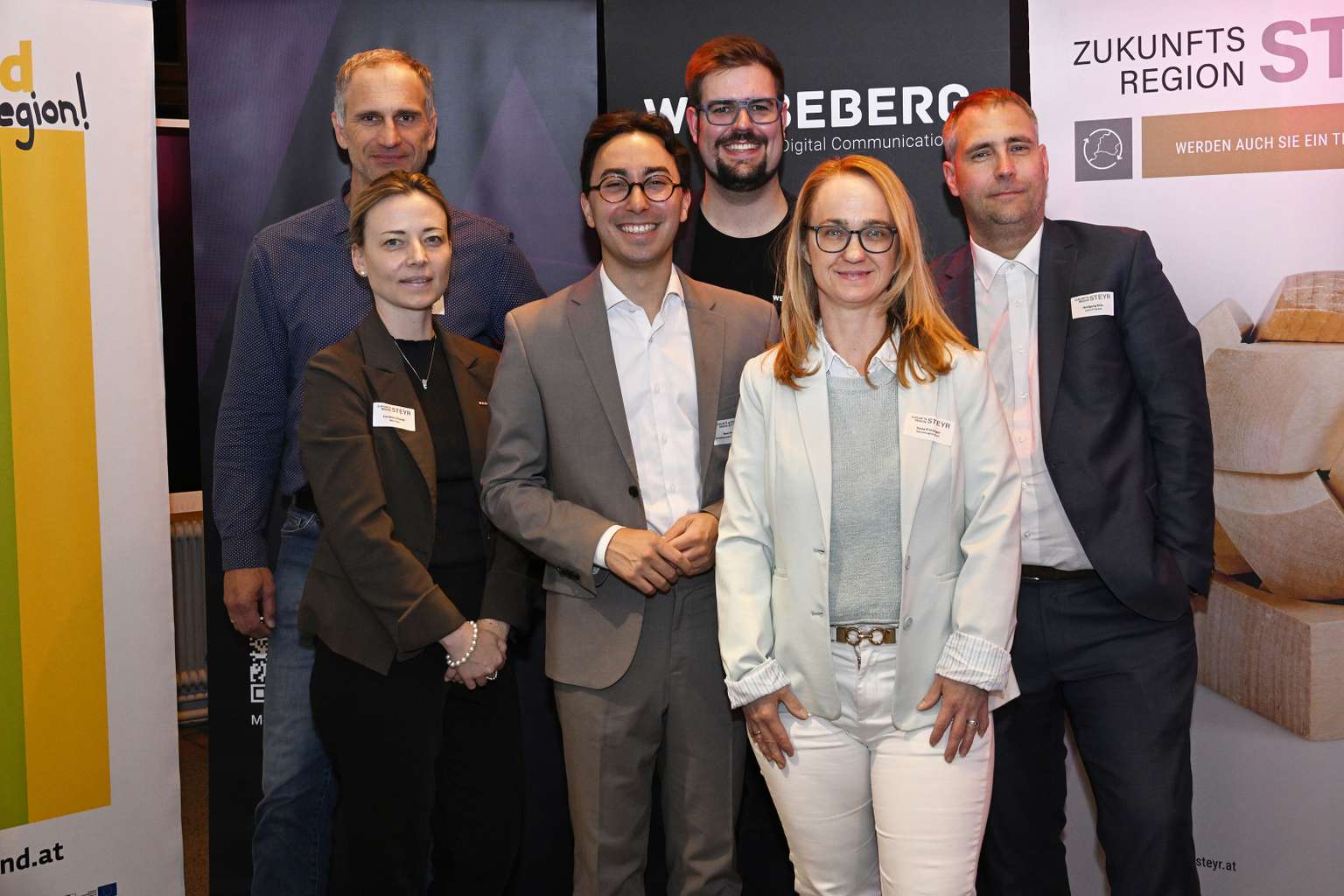 Das Partnerteam aus sechs Personen steht vor den Veranstalterrollups und lächelt in die Kamera.