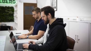 Zwei junge Männer sitzen nebeneinander und arbeiten an ihren Laptops